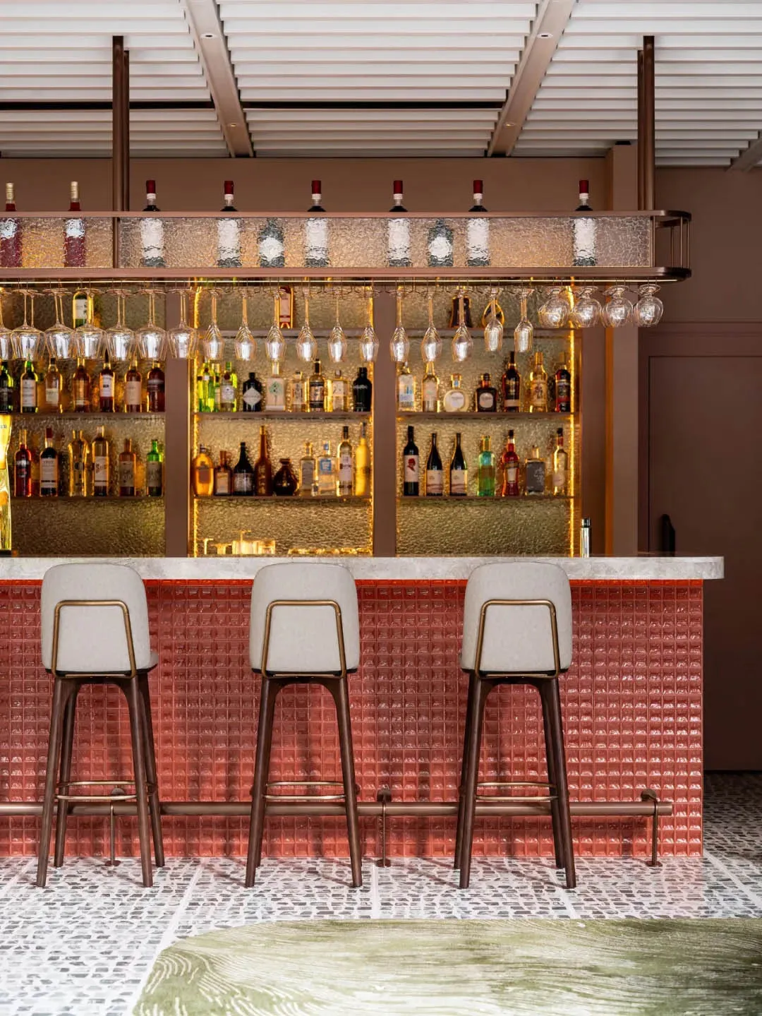 Modern bar interior with glass bottle display and hanging wine glasses.