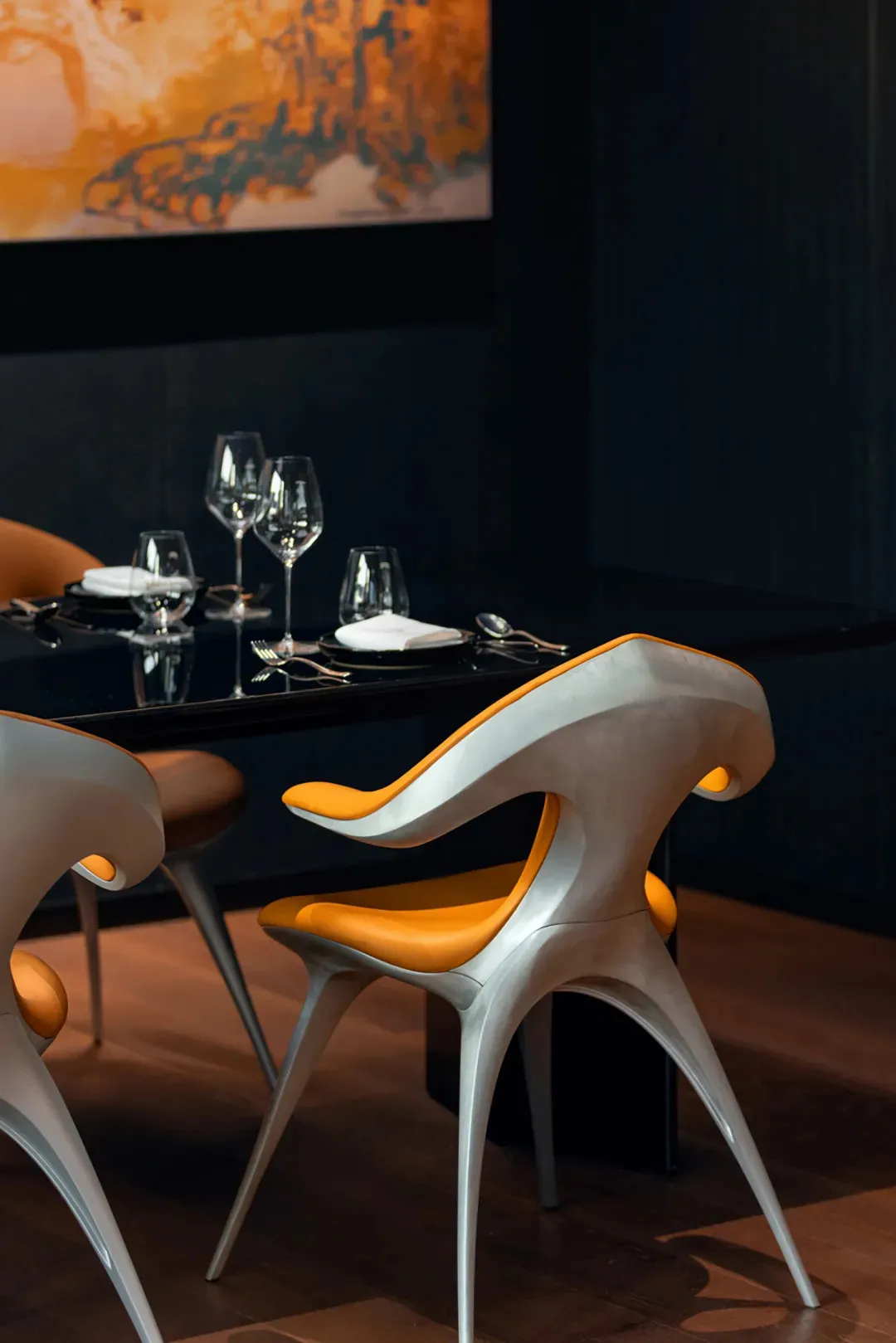 A sleek, modern dining area featuring metallic chairs with orange seats and a dark table, complemented by elegant glassware a
