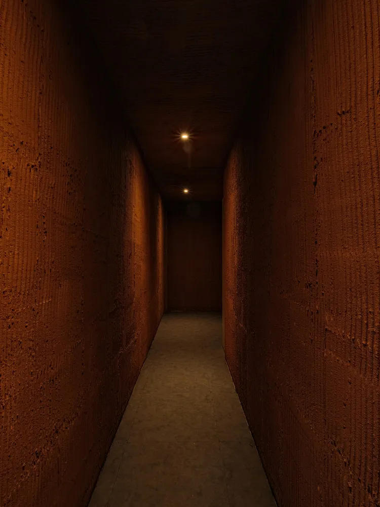 A minimalist tunnel corridor made of concrete, illuminated by two ceiling lights.