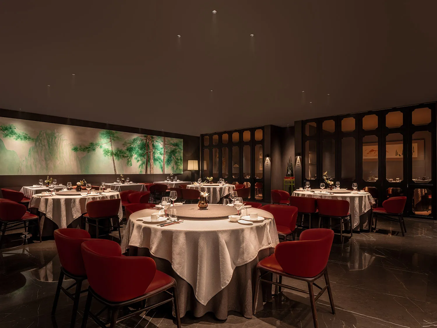 A contemporary restaurant interior featuring tables with white tablecloths and red chairs.