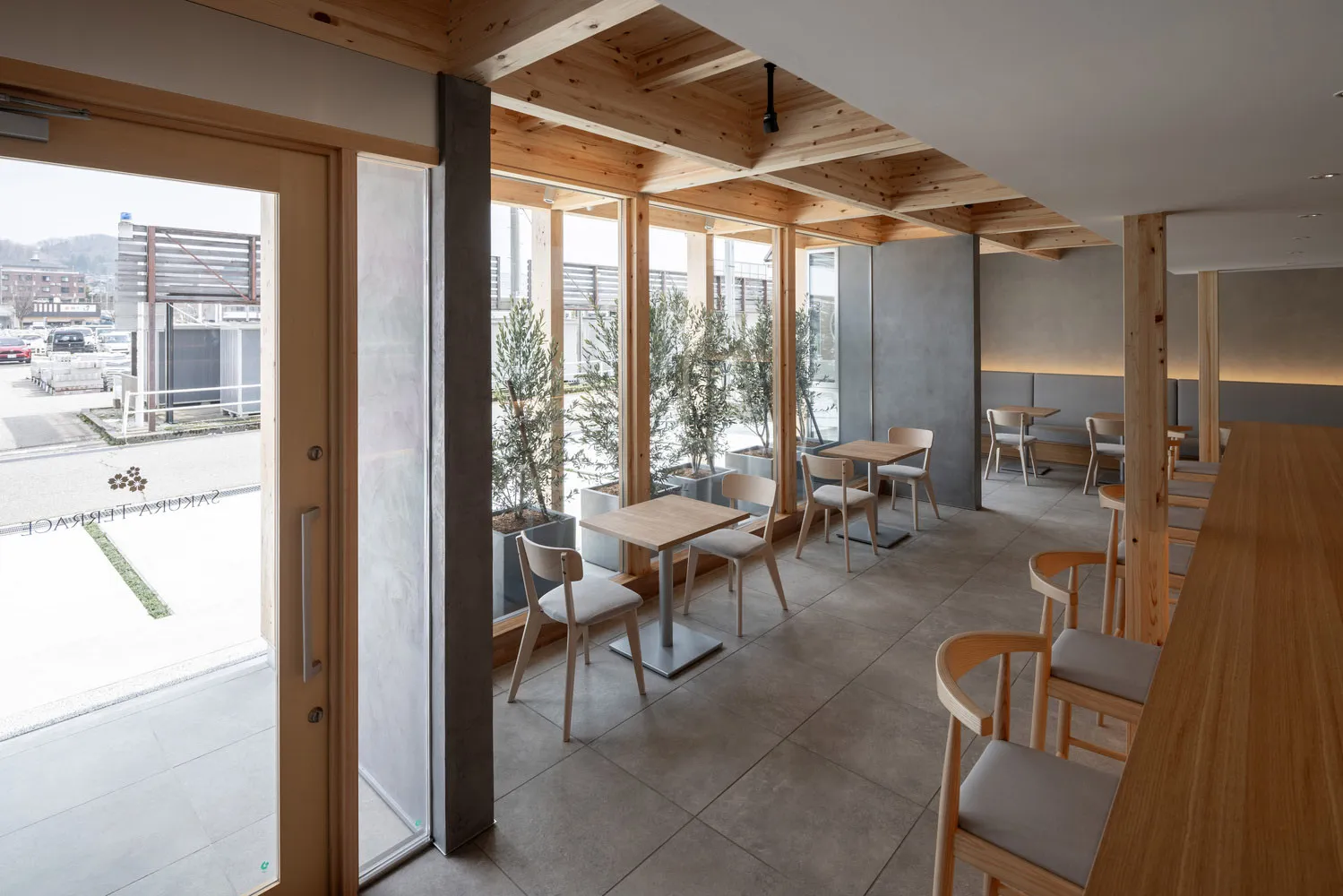 A modern wooden cafe interior with large windows and indoor plants.