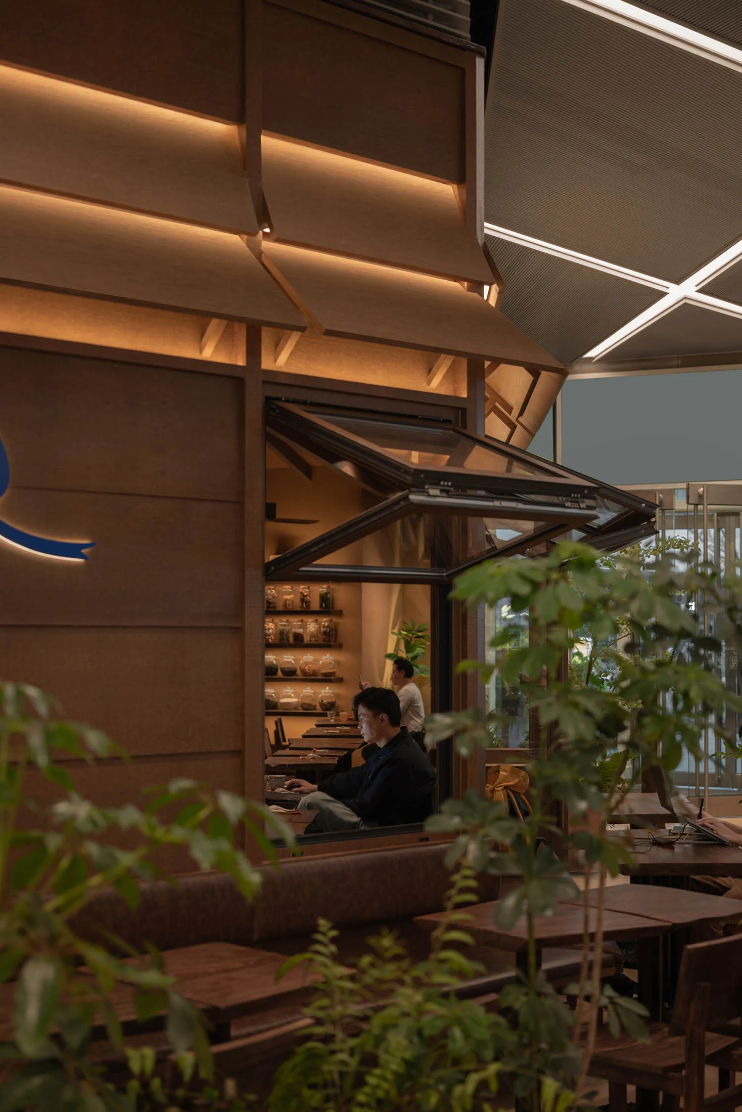 Person working on a laptop in a modern coffee shop with glass walls and wooden furnishings.