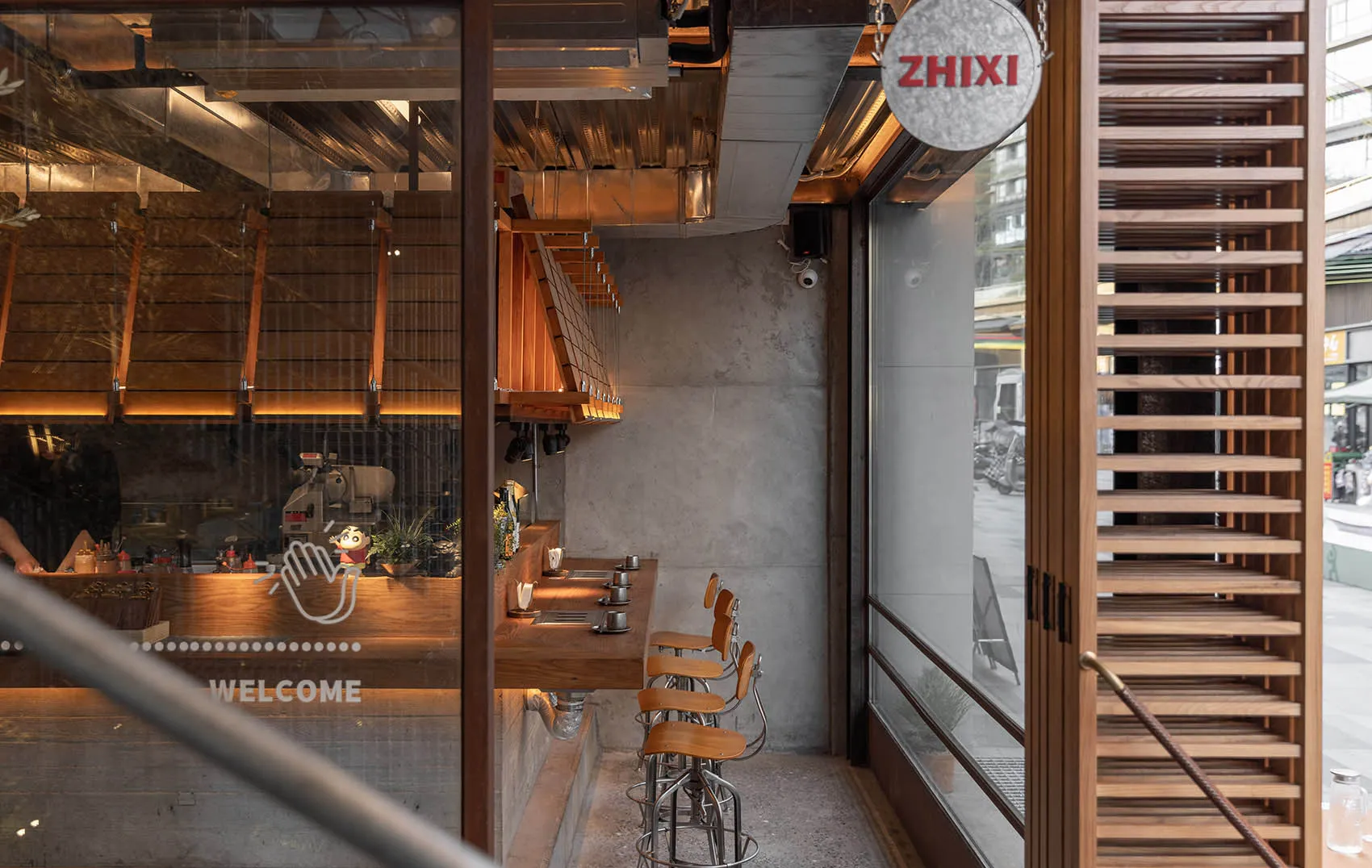 Modern cafe interior featuring a wooden bar counter with stools, industrial lighting fixtures, and a sign displaying 'ZHIXI'.