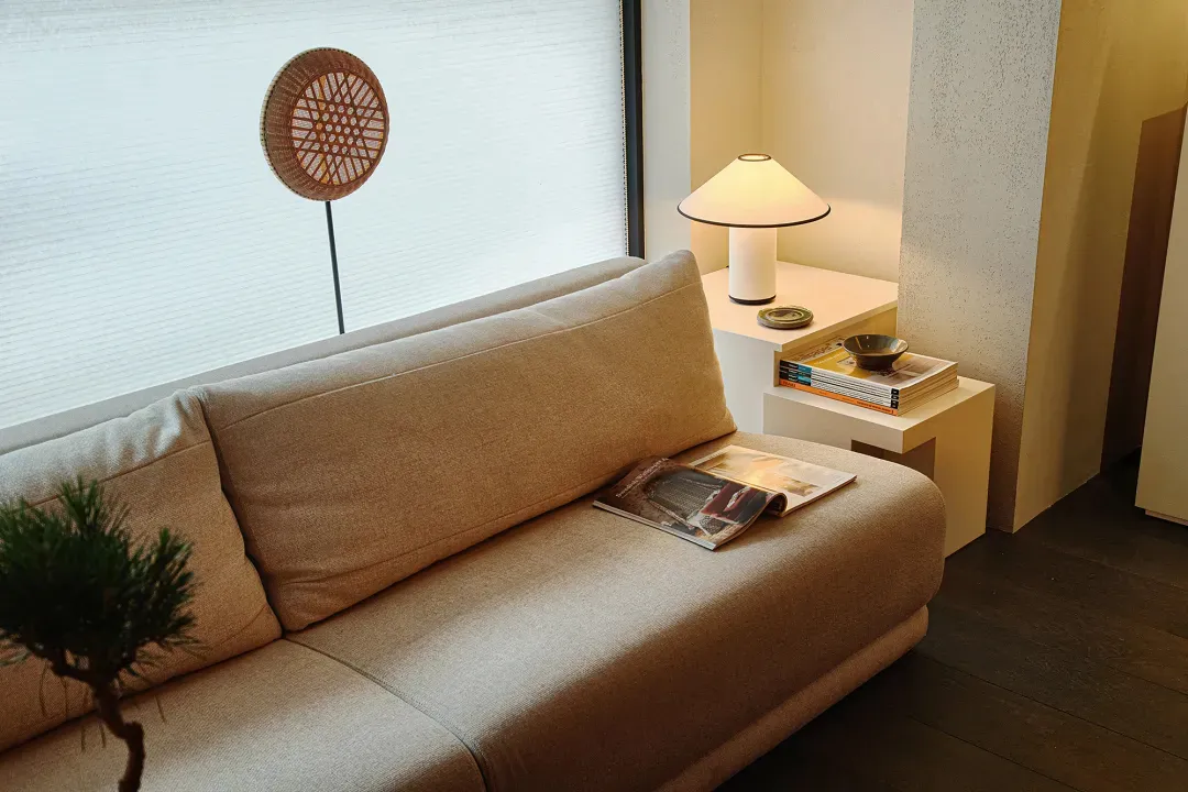 A modern neutral-tones living room with a beige sofa, a table lamp, and magazines.