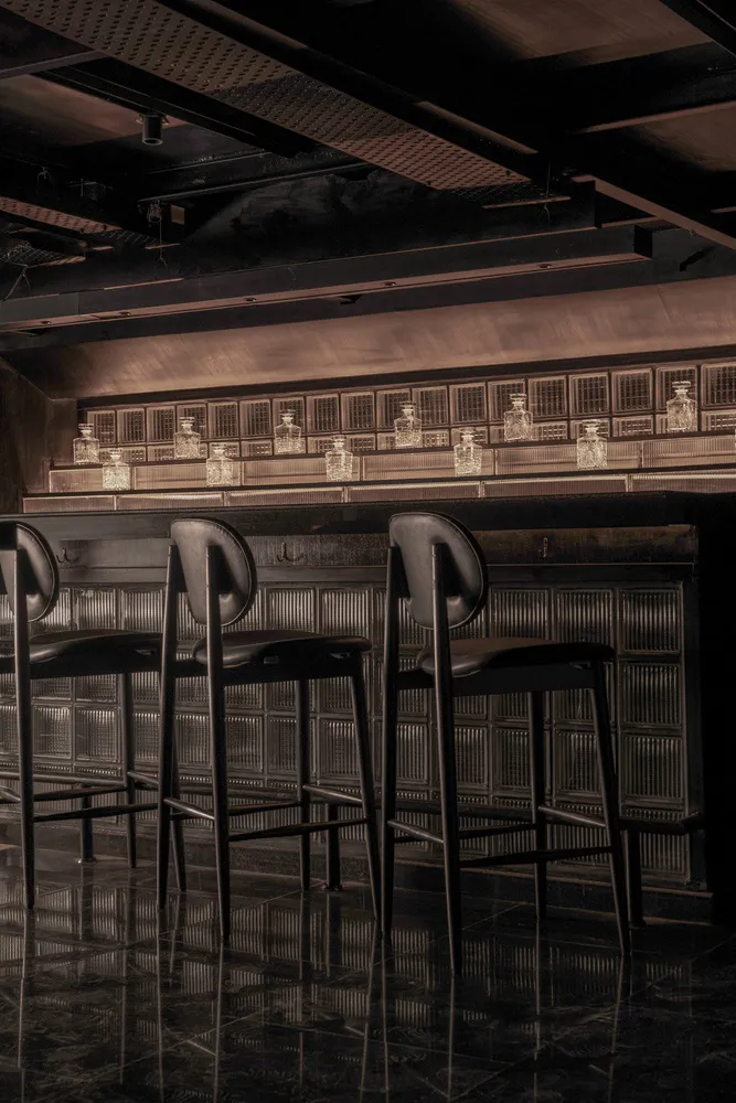 Industrial-style bar with metal stools and a backlit shelf displaying decanters.