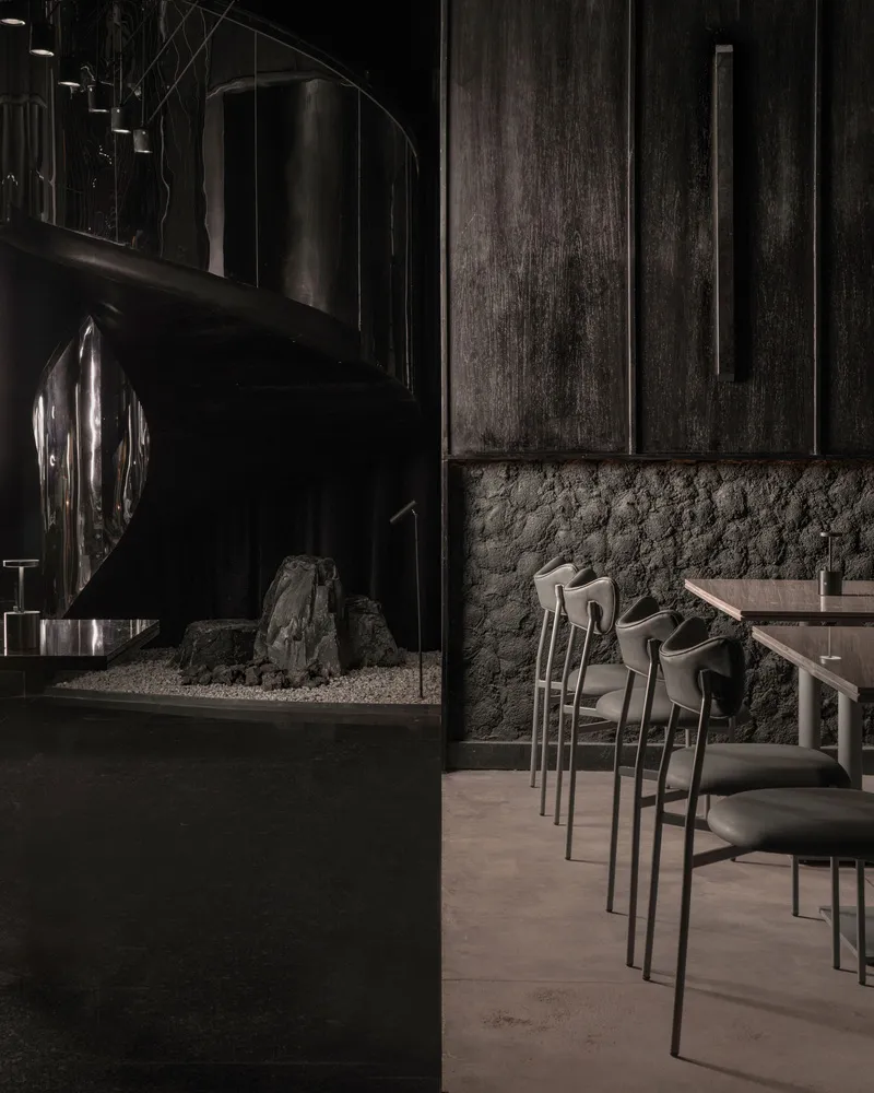 Modern restaurant interior with black walls, steel elements, and concrete floor.