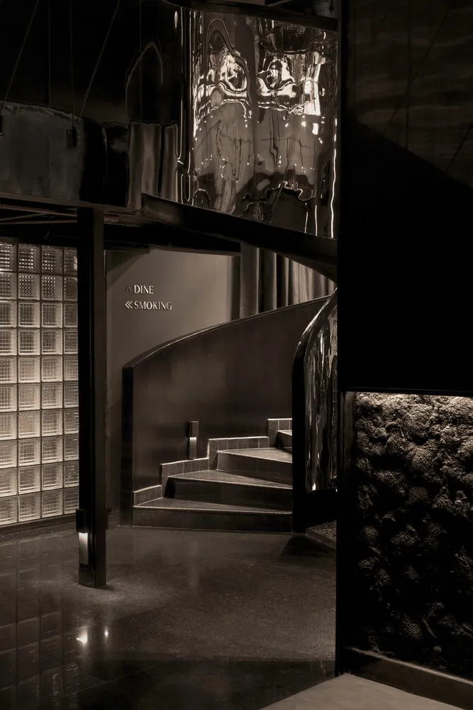 Interior design of a modern restaurant with black stairs and reflective metal wall.