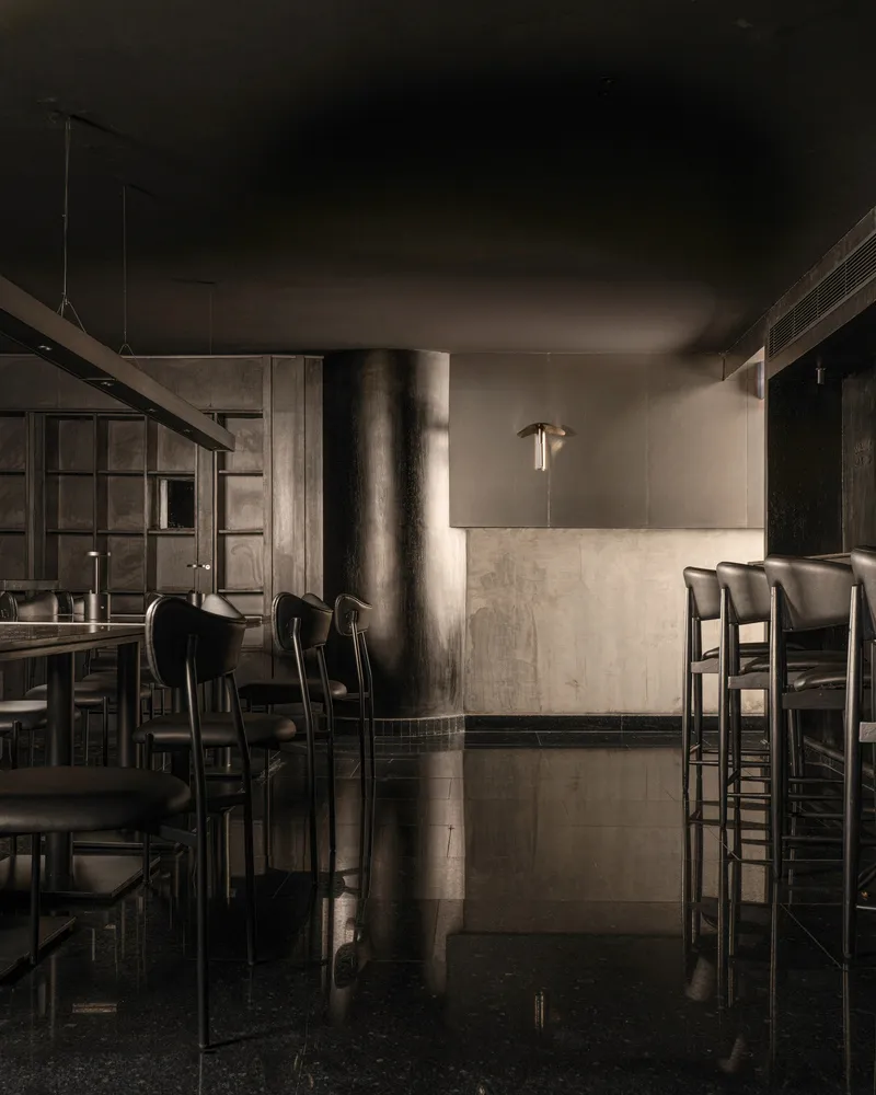 A minimalist, industrial-style restaurant bar with metallic surfaces and black furniture.