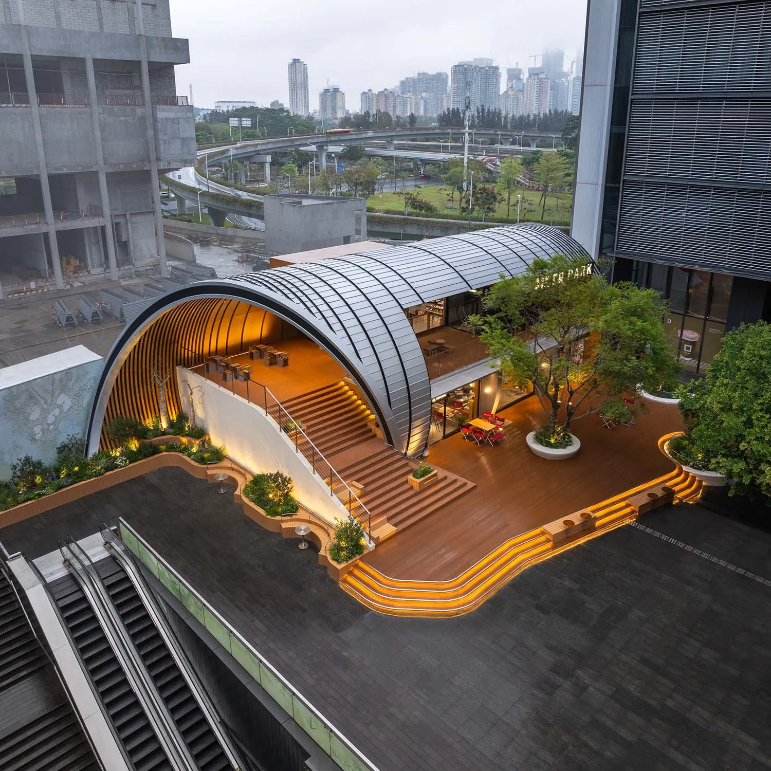 現代公共空間採用金屬與木質結構,搭配弧形入口與綠意植栽。