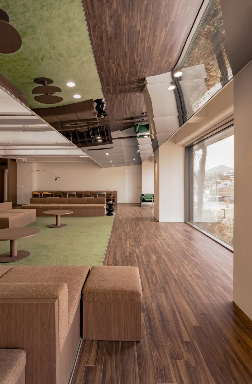 Modern office lounge area with wooden flooring, seating, and green wall.