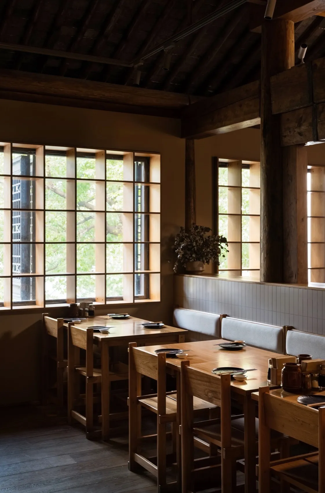 A modern restaurant interior with wooden tables, chairs, and a wooden floor.