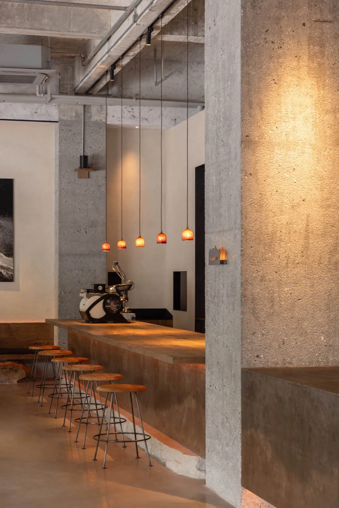 Interior design of an industrial-style coffee shop bar featuring concrete materials and pendant lighting.