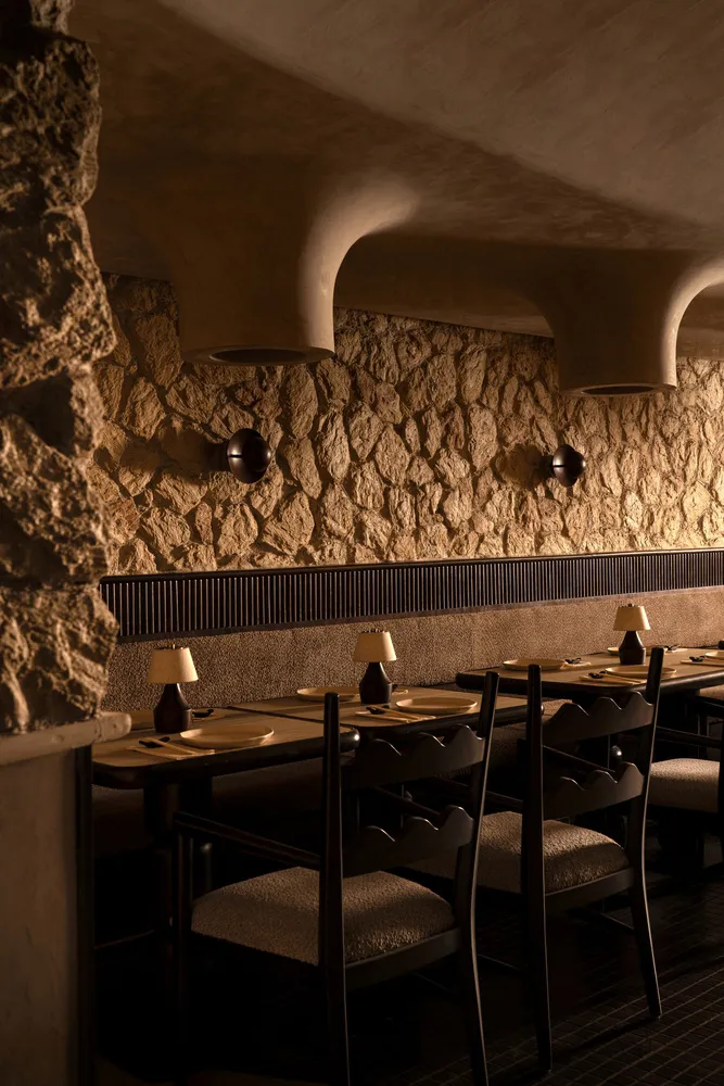 A rustic, industrial dining room with stone and concrete walls, wooden tables, and minimalist decor.