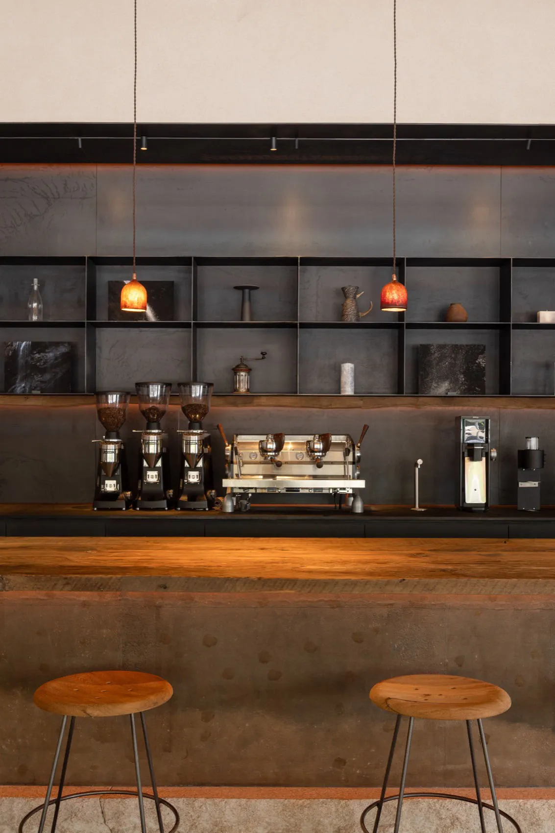 A modern coffee shop interior with a wooden counter, concrete wall, black metal shelving, and coffee-bar setup.