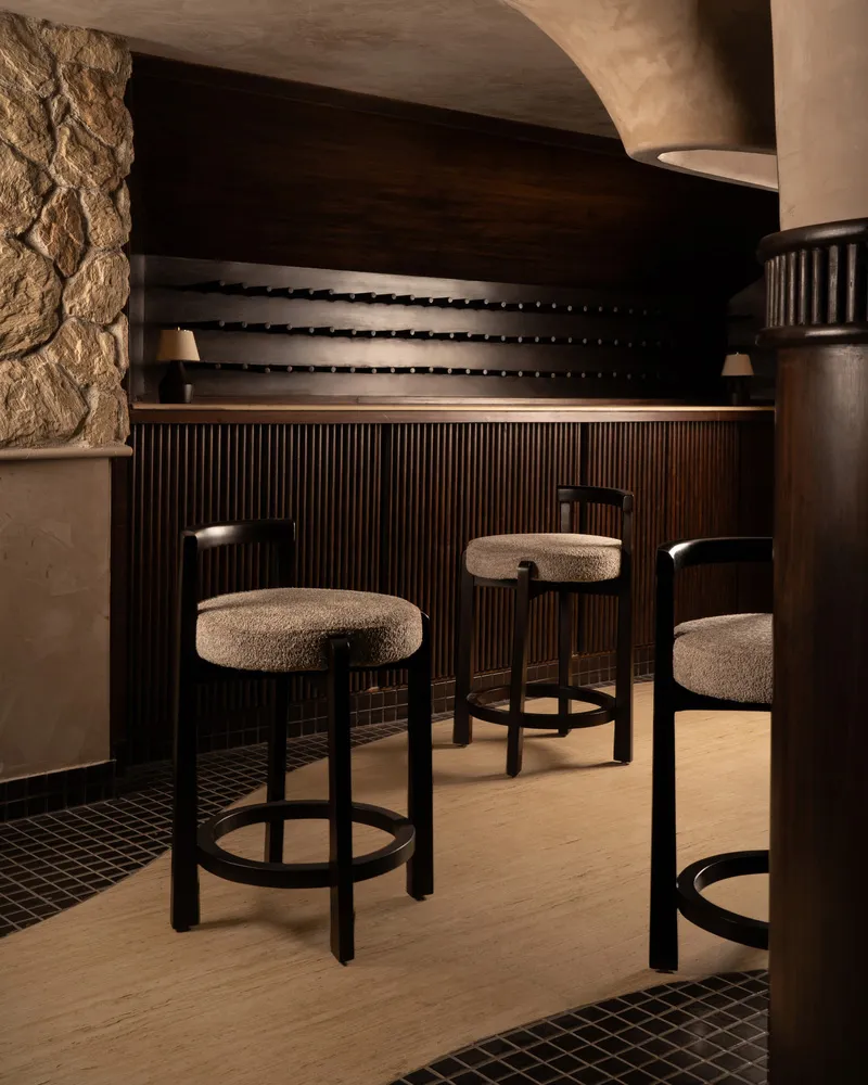 A modern bar counter featuring a wine rack and upholstered stools near a stone wall.