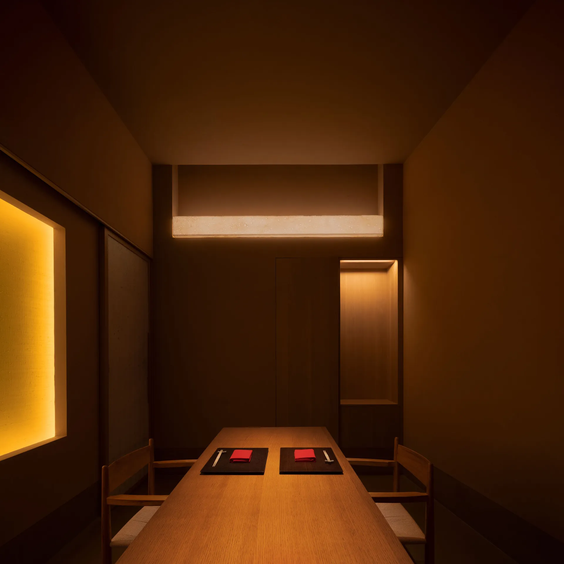 A modern restaurant dining room illuminated by warm, ambient lighting, featuring wooden furniture and minimalist decor.