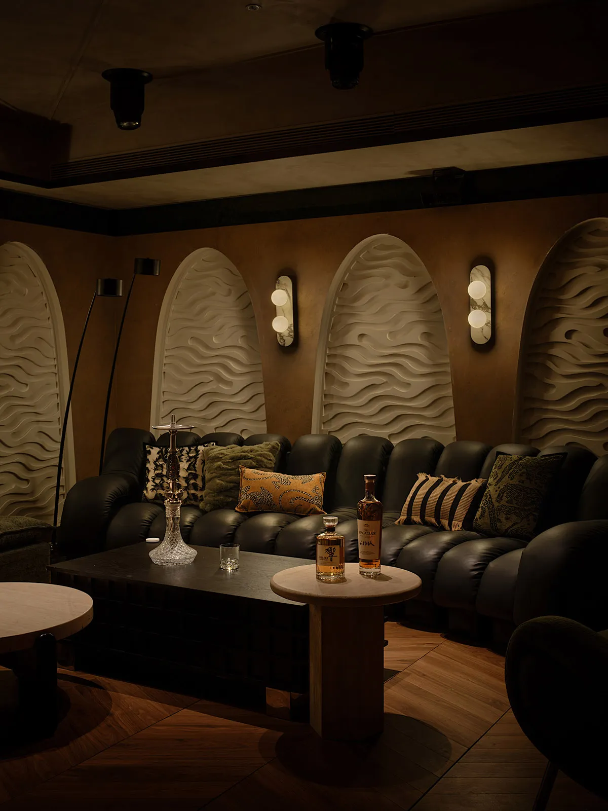 A modern living room with black leather sofas, cabinets, and arched textured panels.