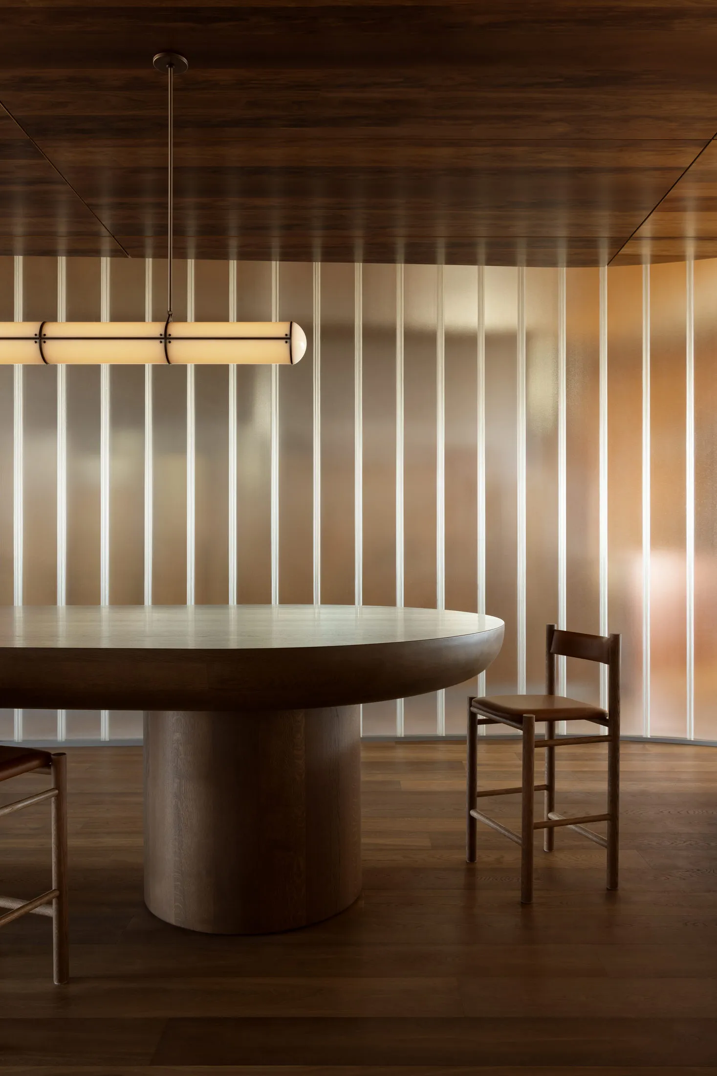 A modern dining room featuring a round wooden table with a fiber-glass table top, accompanied by wooden chairs with leather s