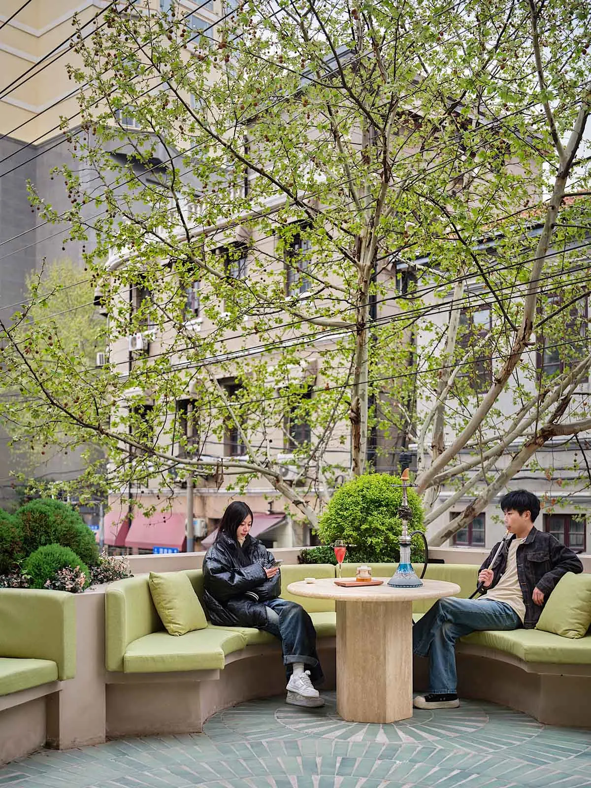 Two individuals sitting at a round table in a modern restaurant with concrete furnishings and greenery.