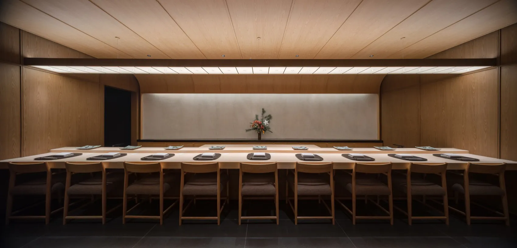 Modern minimalist restaurant interior featuring a long wooden table with place settings and a floral centerpiece.