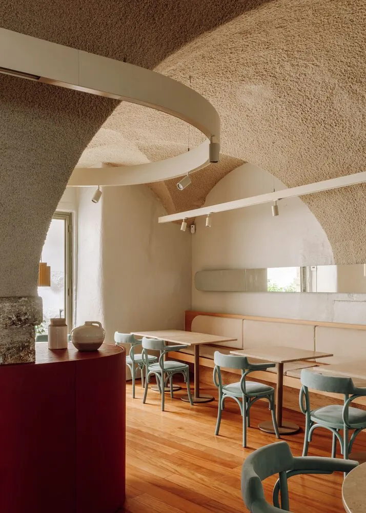 A modern cafe interior with concrete walls, wooden flooring, and teal dining chairs