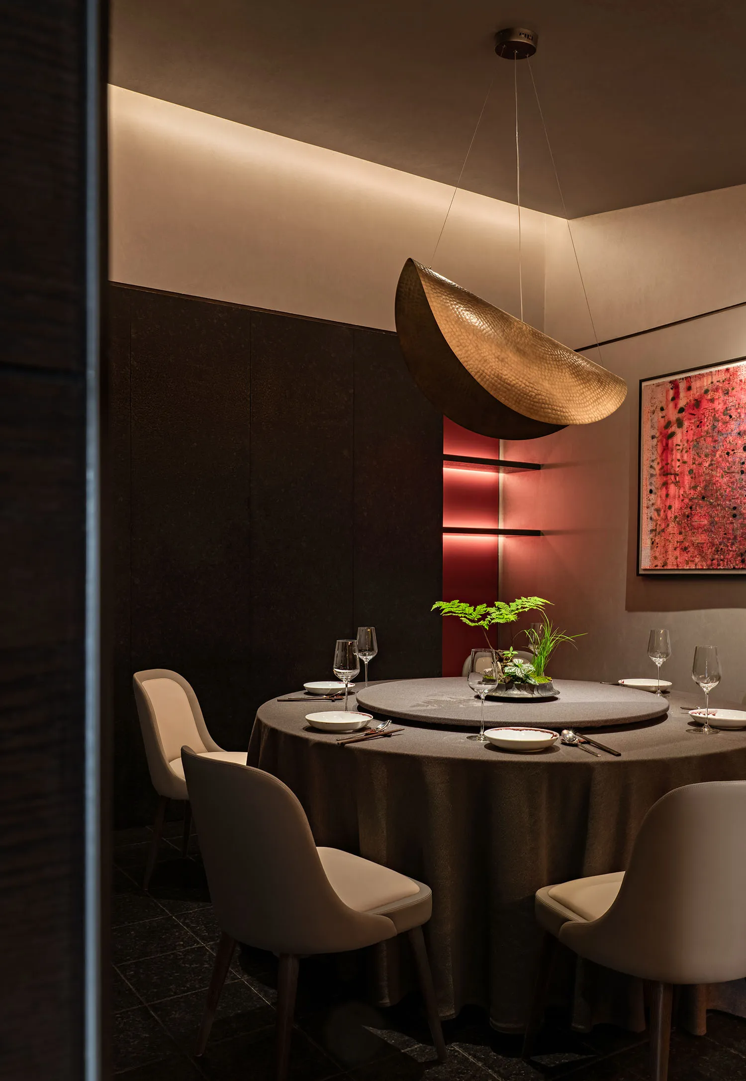A modern restaurant interior with metallic pendant lighting and red lighting accents.