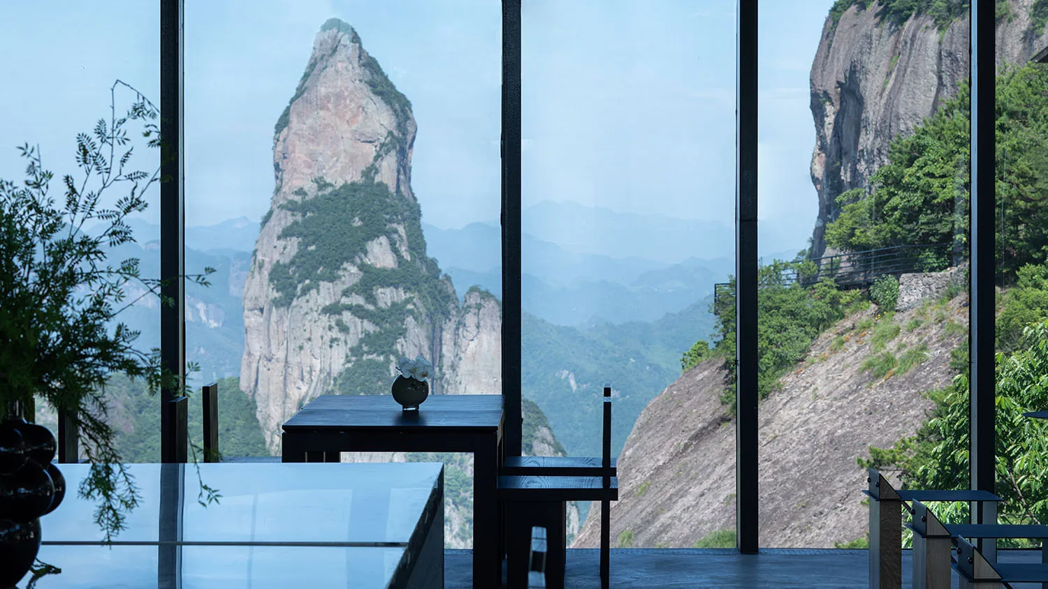A modern restaurant interior with glass walls overlooking a scenic mountain view.