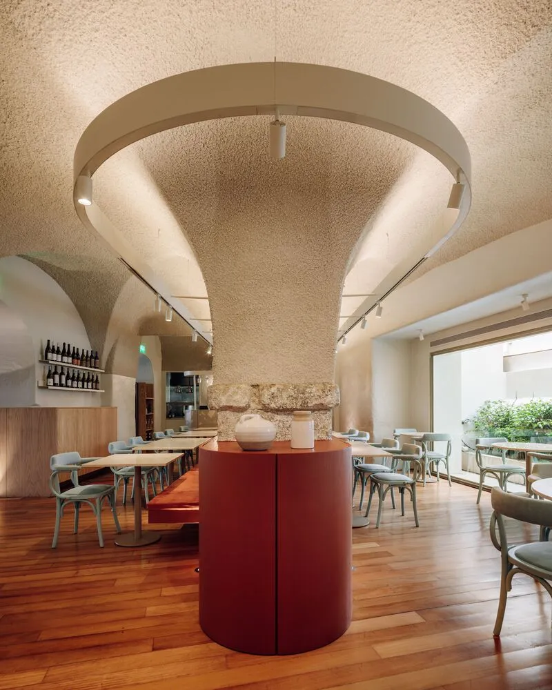Modern restaurant interior with wooden furniture, concrete pillars, and glass elements, featuring minimalist design.