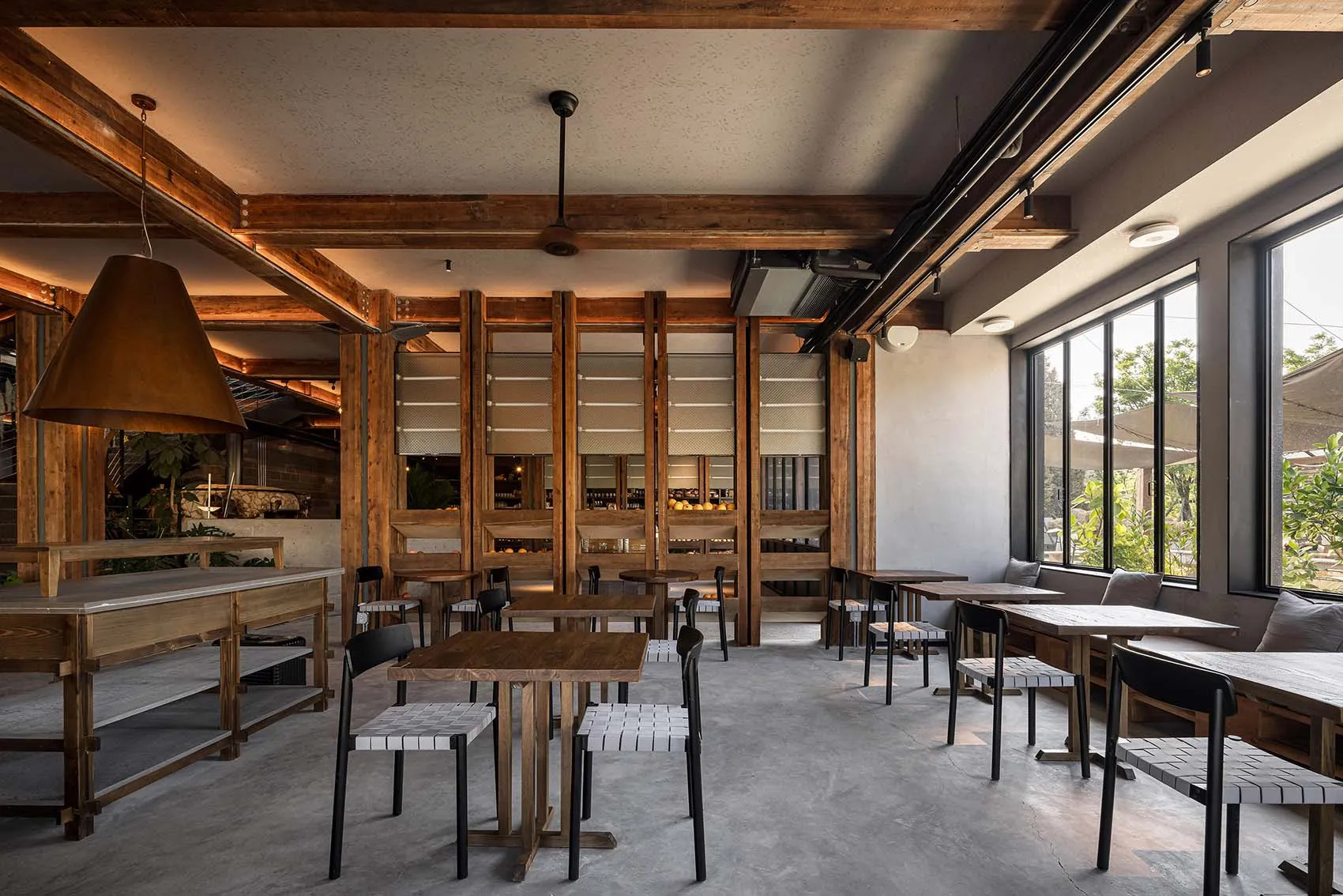 A modern industrial-style coffee shop interior with wood tables and chairs, concrete floor, and large windows.