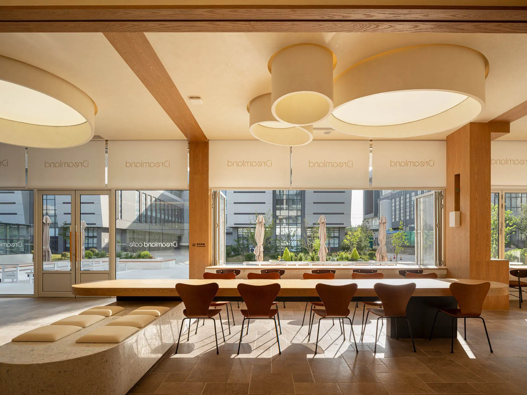 A modern cafe interior with wooden tables and chairs, round pendant lights, and large windows.