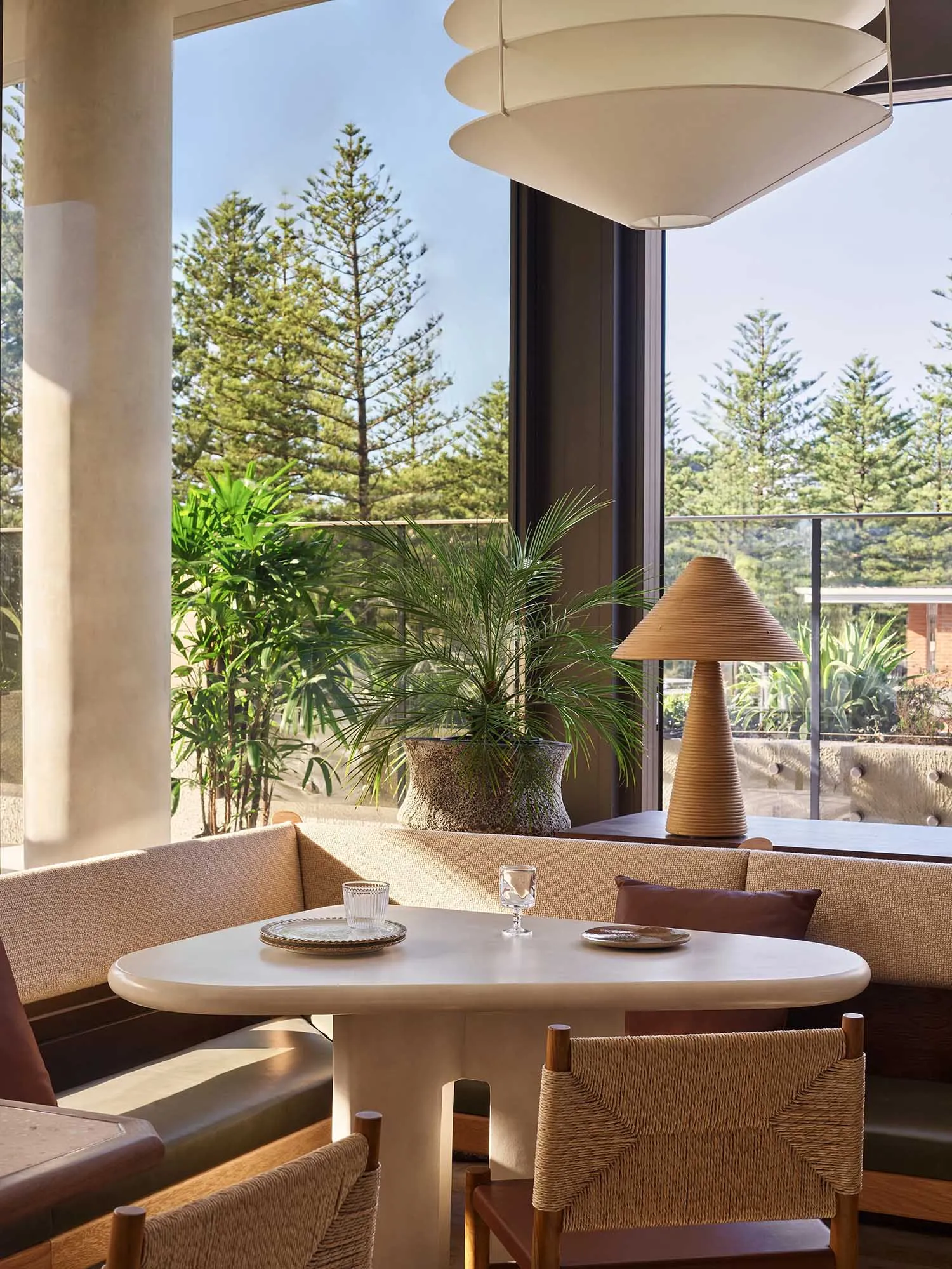 A modern restaurant interior with natural light, comfortable seating, and greenery.