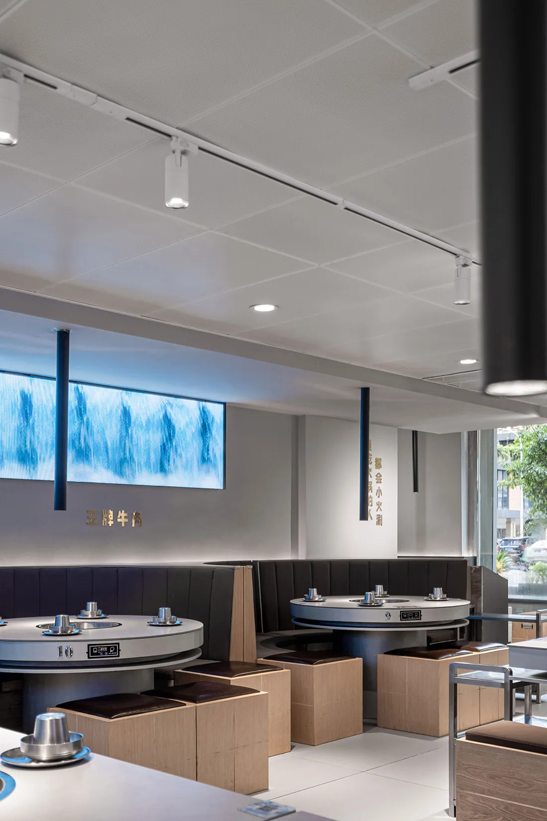 A modern restaurant interior with wooden tables, metal booths, and fabric seating.
