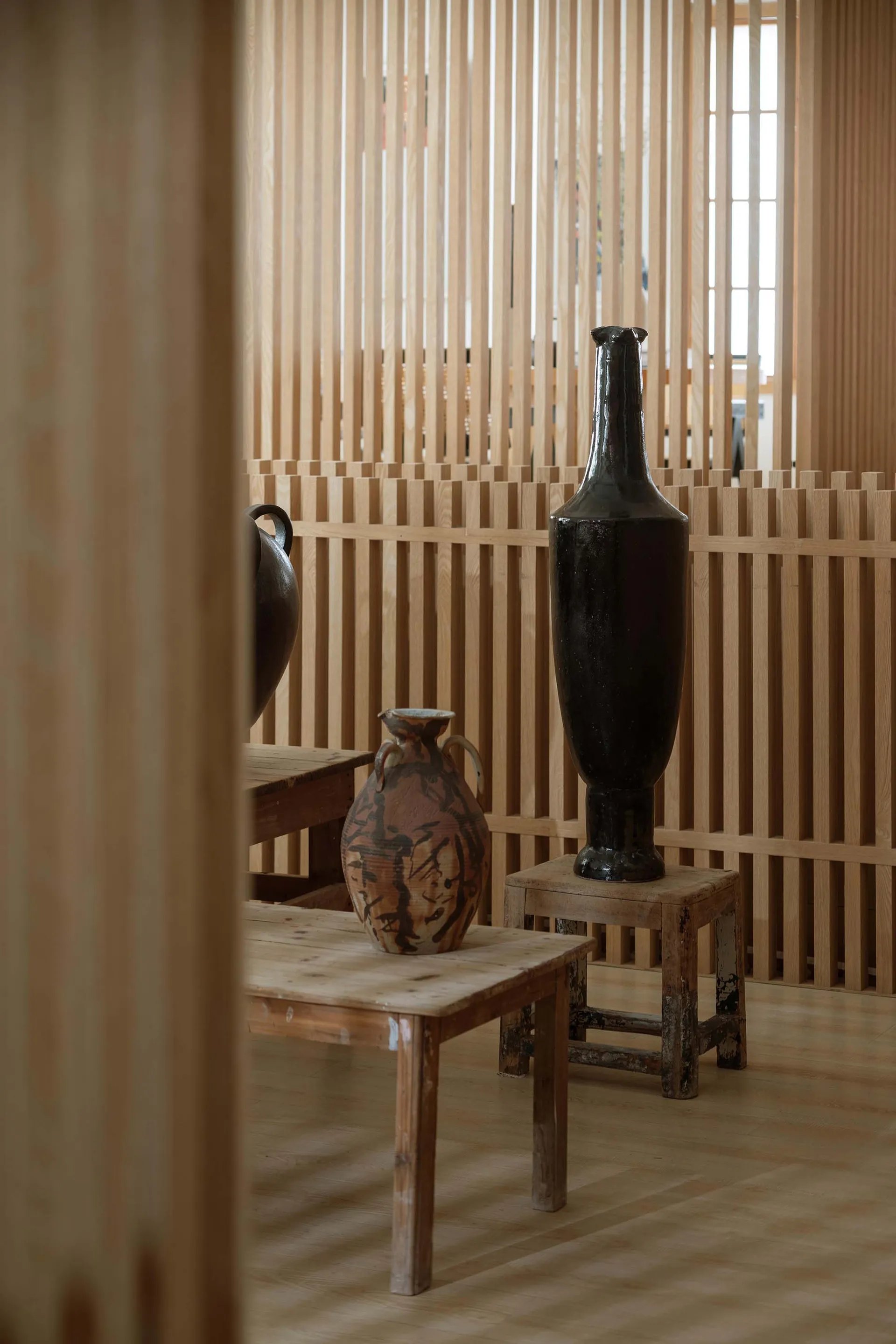 Decorative ceramic vases placed on wooden stools and tables in a room with wooden slat walls.