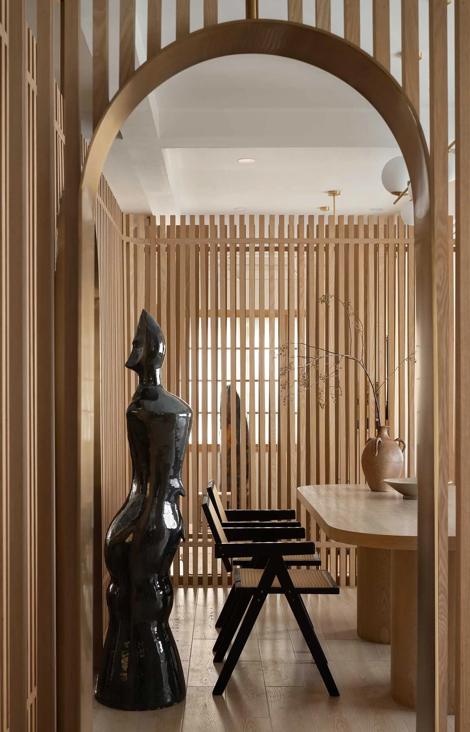 A modern dining room featuring timber slat dividers, black chairs, and a black statue.