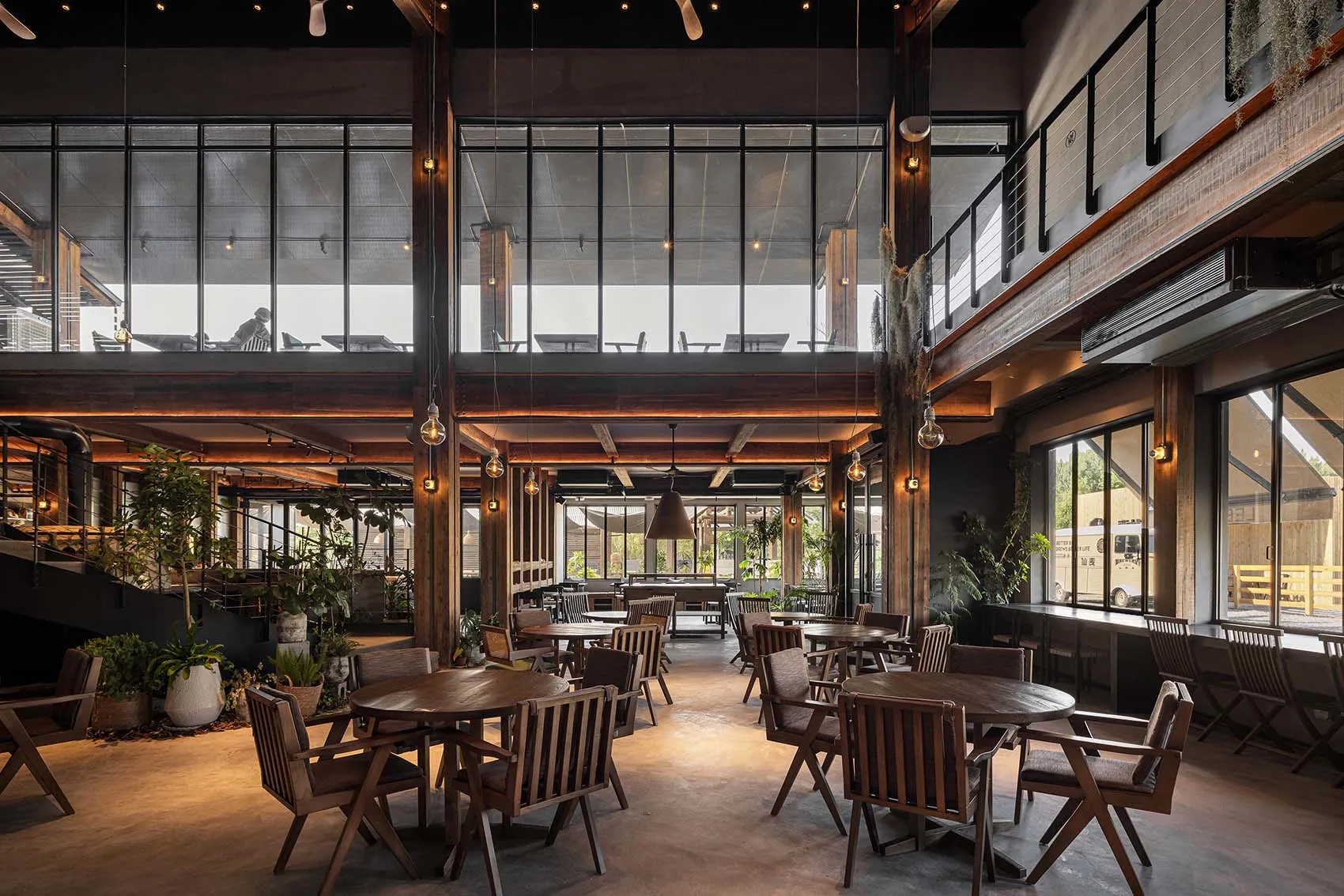 Modern industrial-style cafe with wooden tables, concrete flooring, and glass walls.