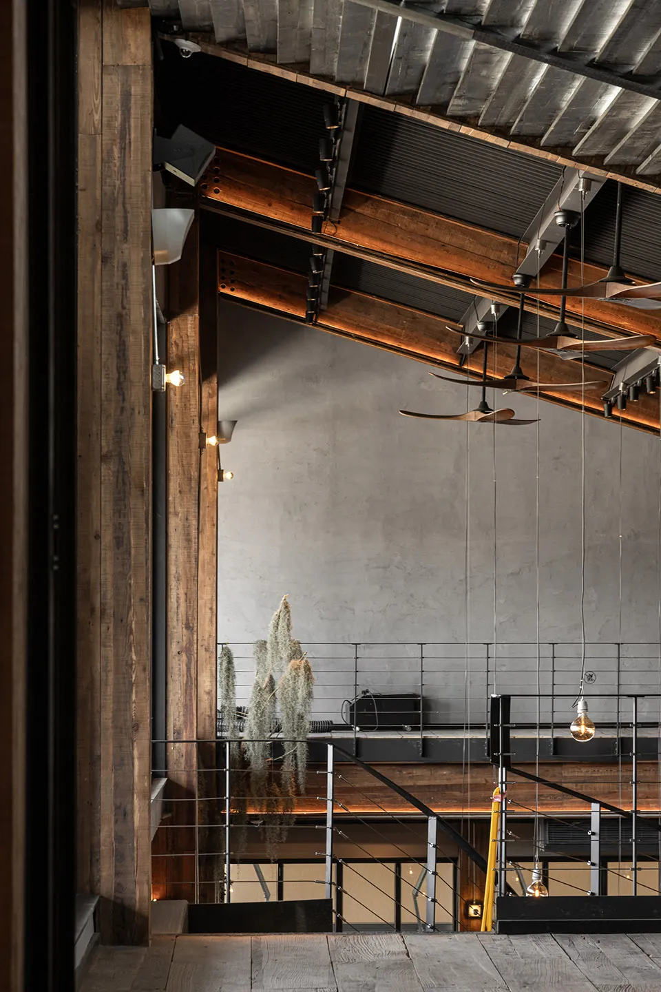 Industrial-style restaurant interior with wooden beams, concrete walls, and ceiling fans