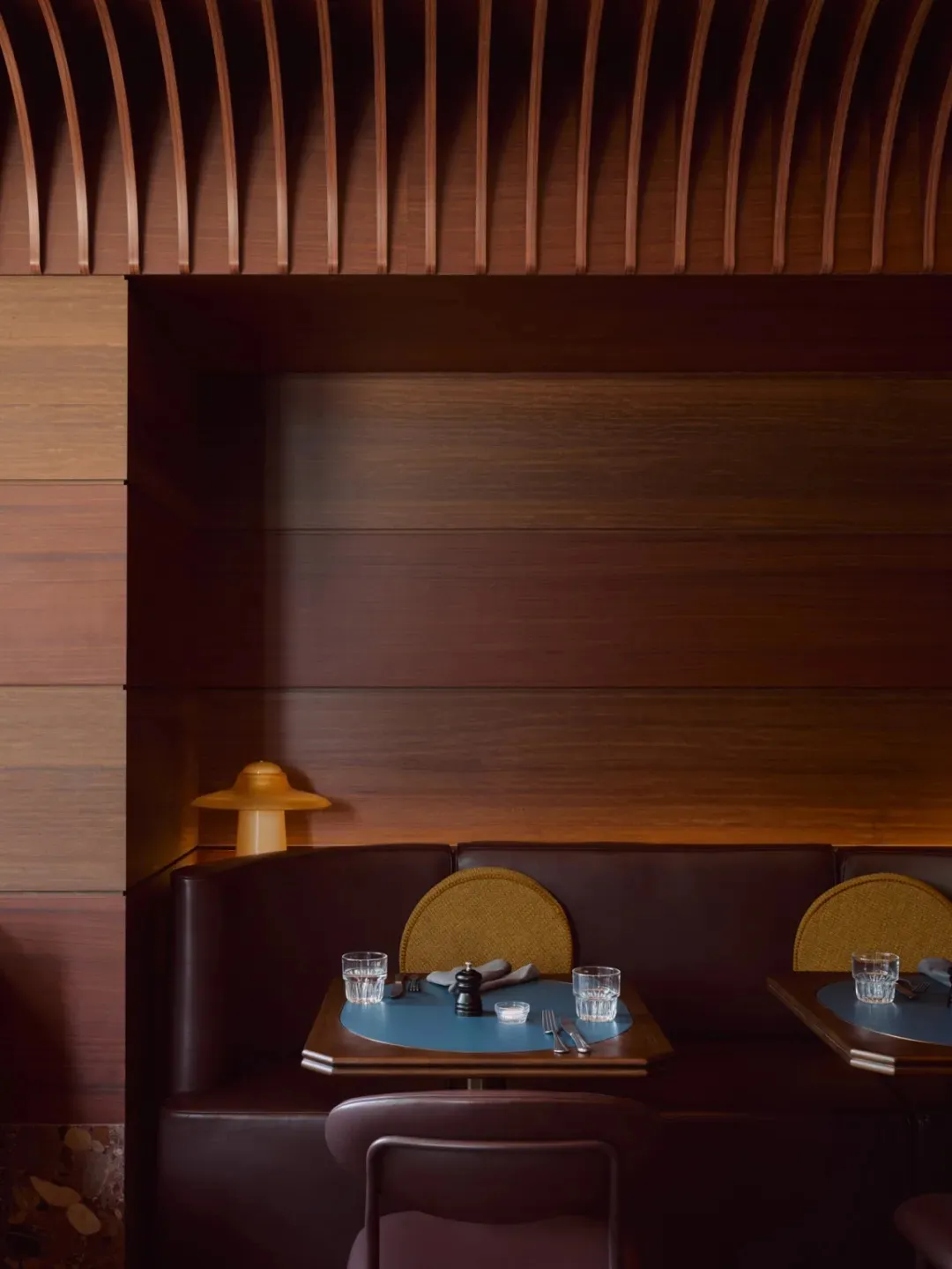 A modern restaurant booth made of wood with a sleek design, featuring plush seating and a small table with glasses and cutler