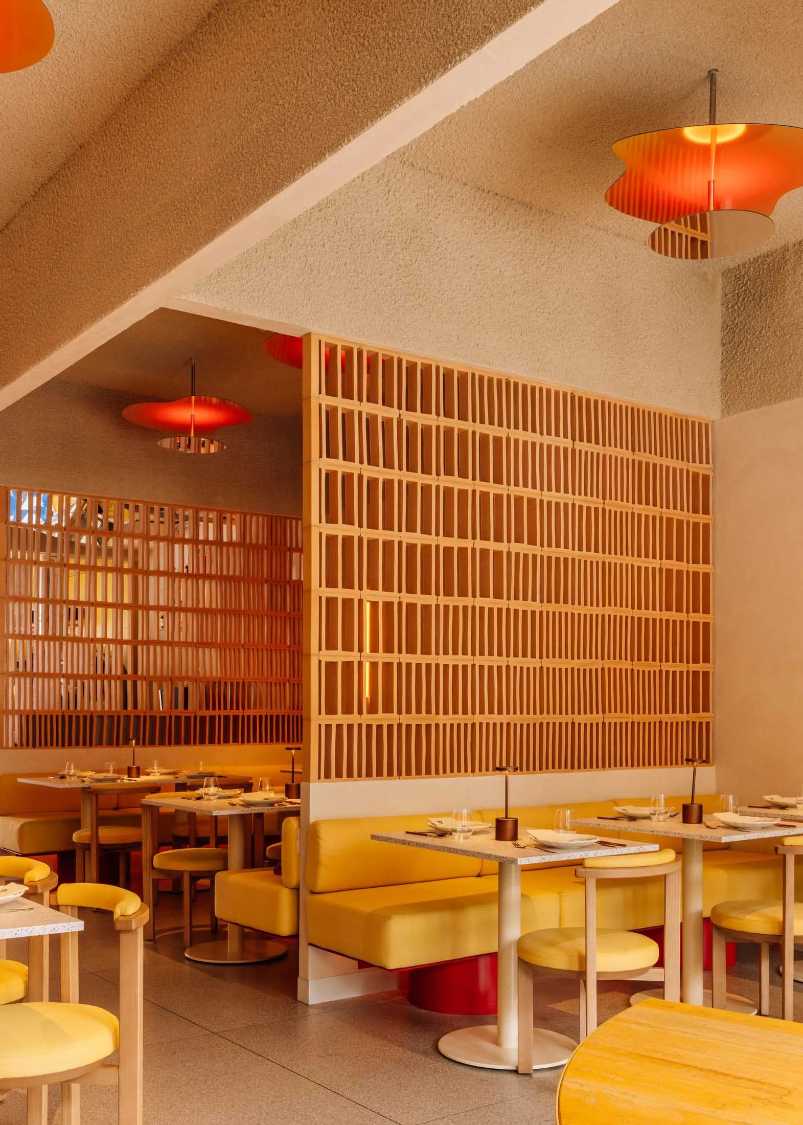 Modern restaurant interior with yellow seating, wooden accents, and red pendant lights