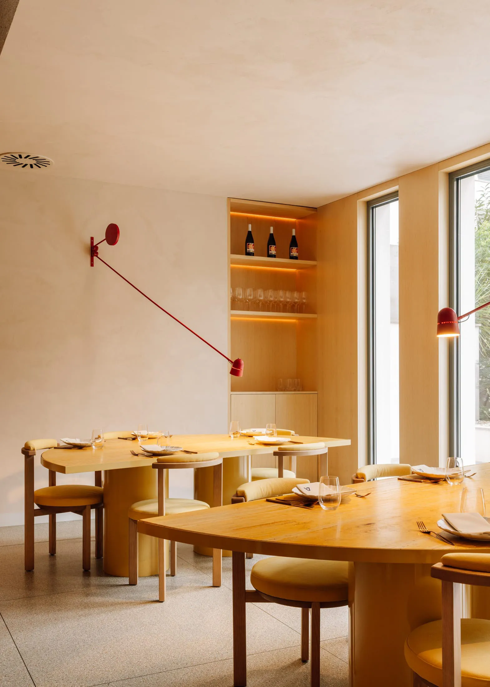 Modern restaurant interior featuring wooden tables and chairs with concrete flooring and walls.