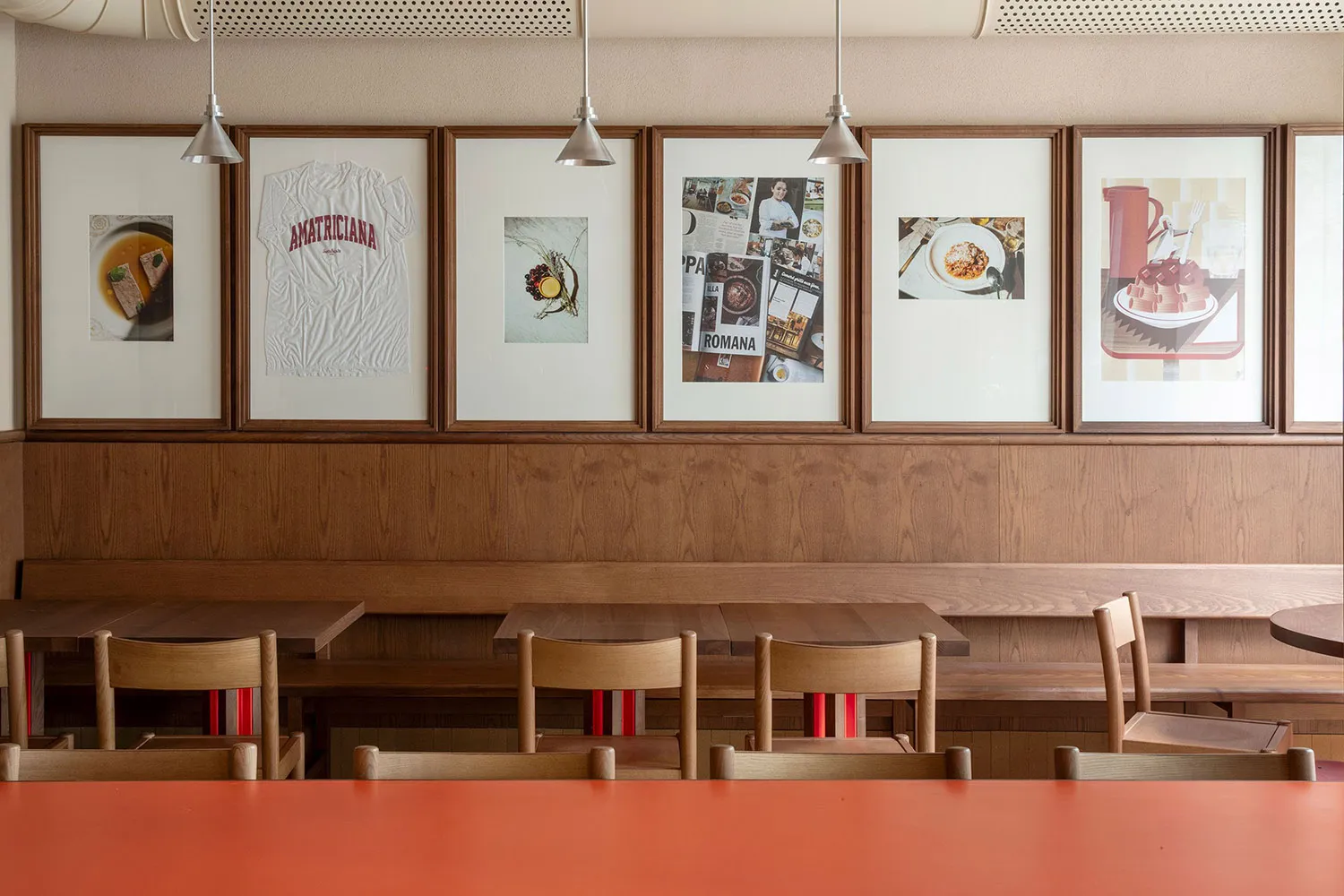 A modern restaurant interior featuring wooden tables, chairs, and benches with framed artworks on the wall.