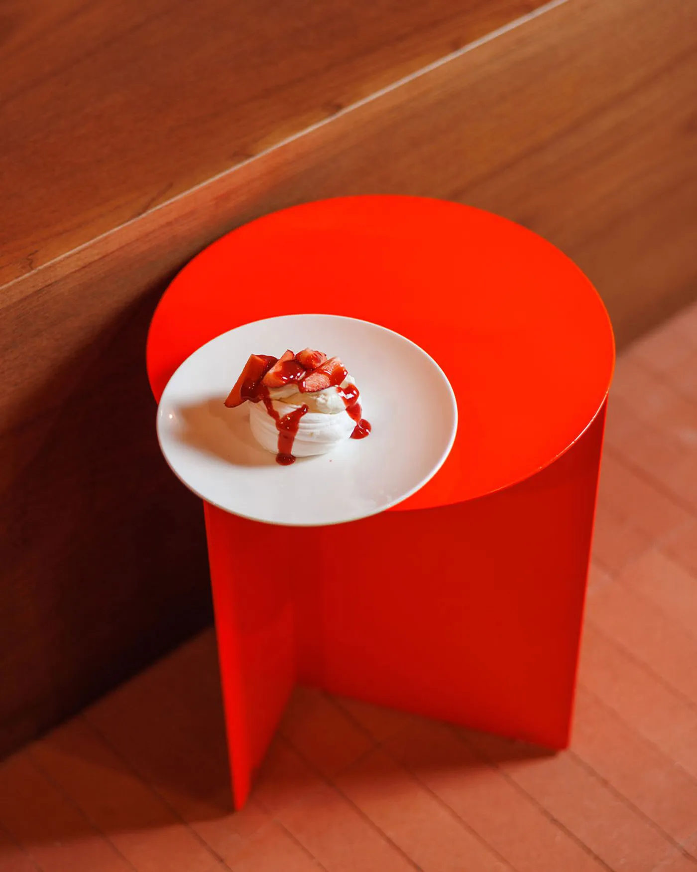 A metallic red table with a white plate containing a dessert with strawberries and a drizzle of sauce.