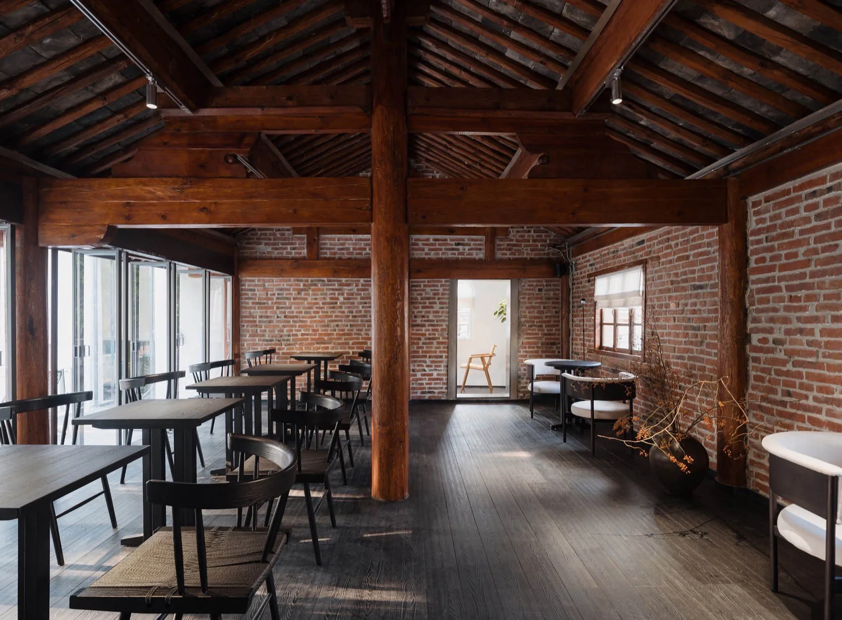 Industrial-style restaurant interior with wooden tables, brick walls, and exposed wooden beams on the ceiling.