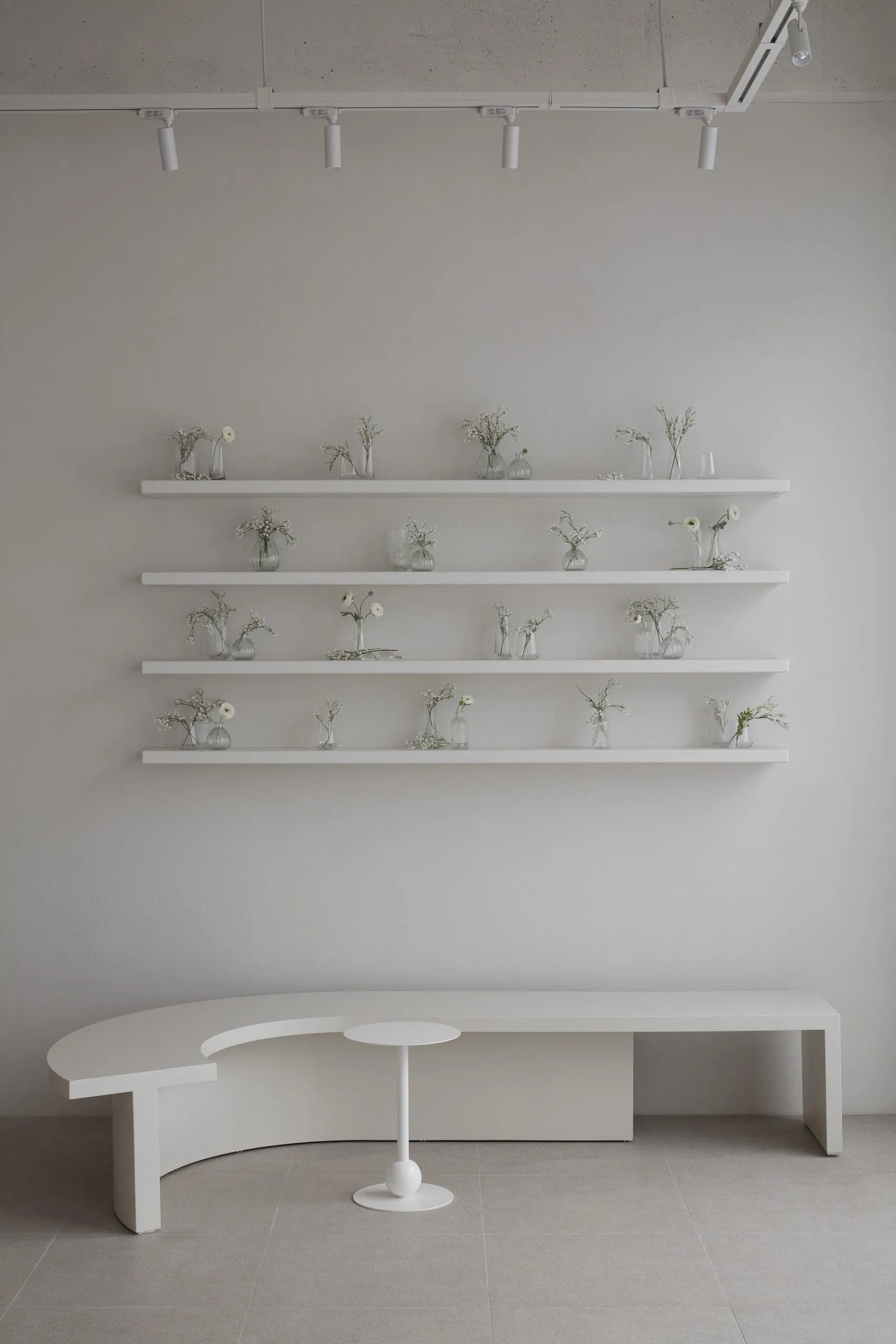 A minimalist interior space featuring a concrete bench with a small table and shelves adorned with white floral arrangements.