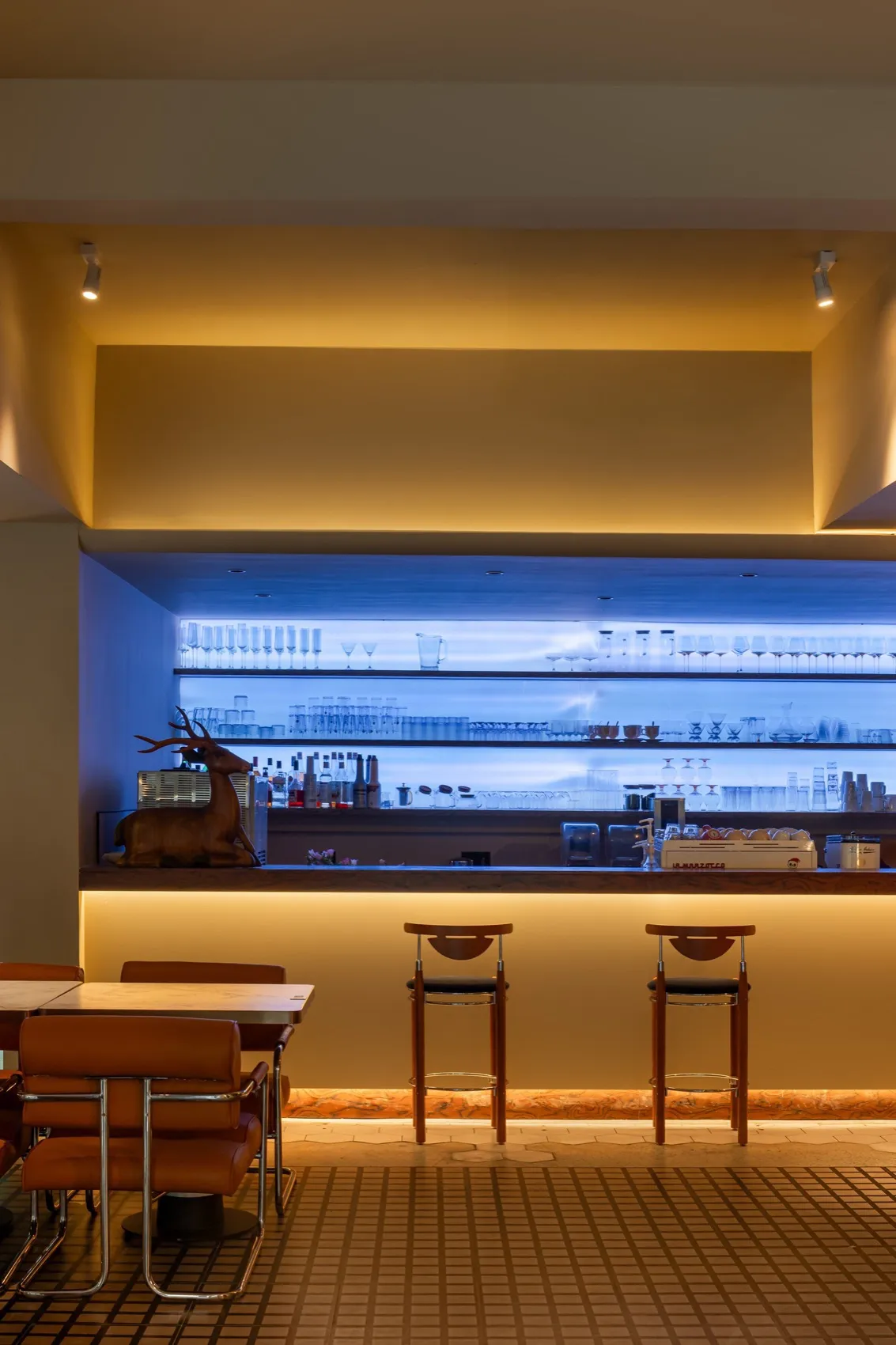 A stylish modern restaurant bar with wooden furniture, glass shelves, and concrete accents.