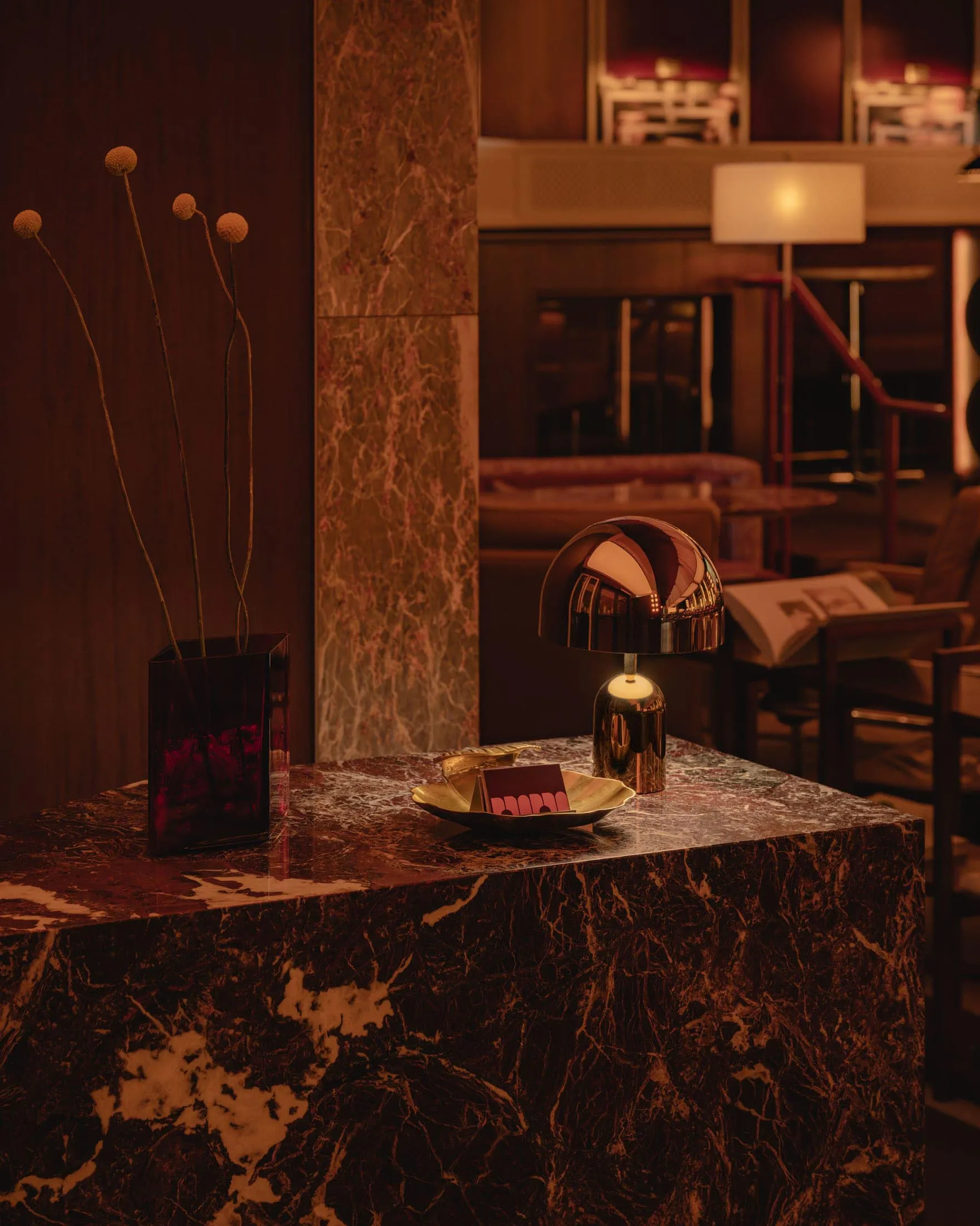 A modern living room with a marble table featuring a spherical lamp and a vase with dried flowers.
