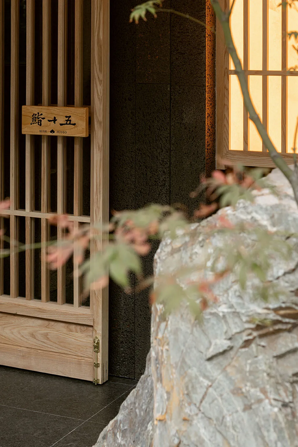 A minimalist restaurant entrance featuring wooden sliding doors and a rock garden.