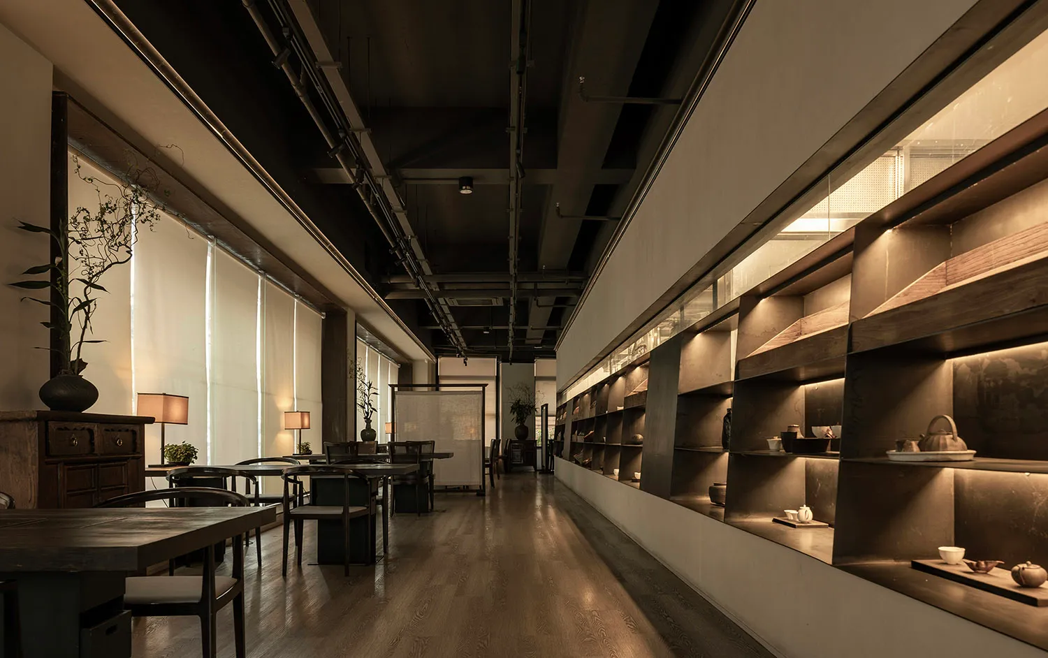 Long shot of a modern restaurant interior with wooden tables, chairs, and concrete walls.