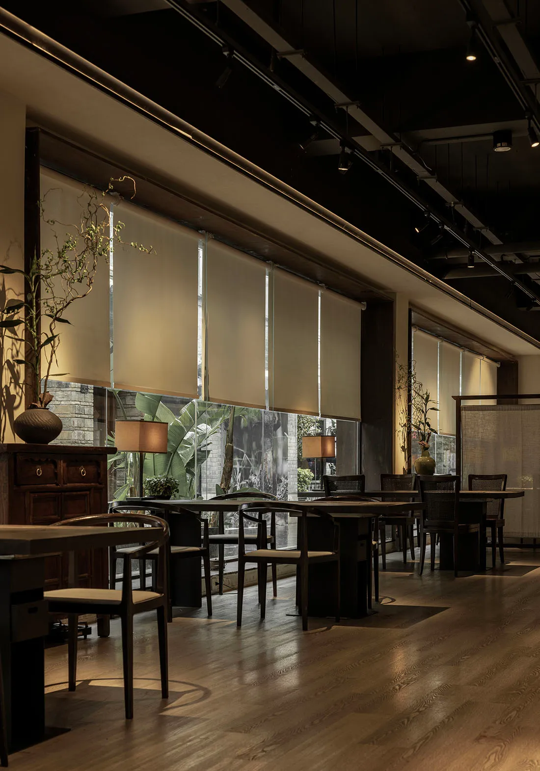 Interior of an industrial-themed restaurant with wooden tables and chairs, glass walls, and natural light.