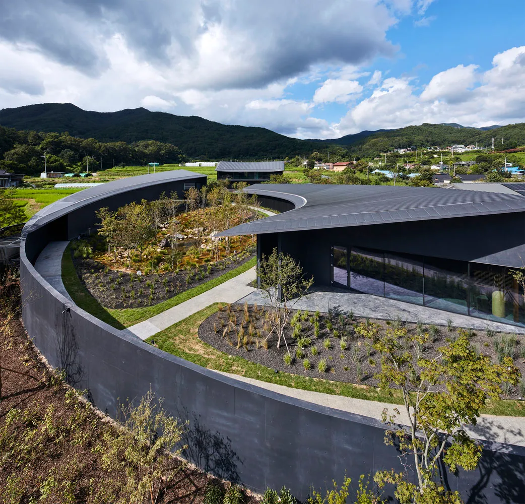Modern architectural design featuring a concrete structure with curved rooflines and greenery landscape.