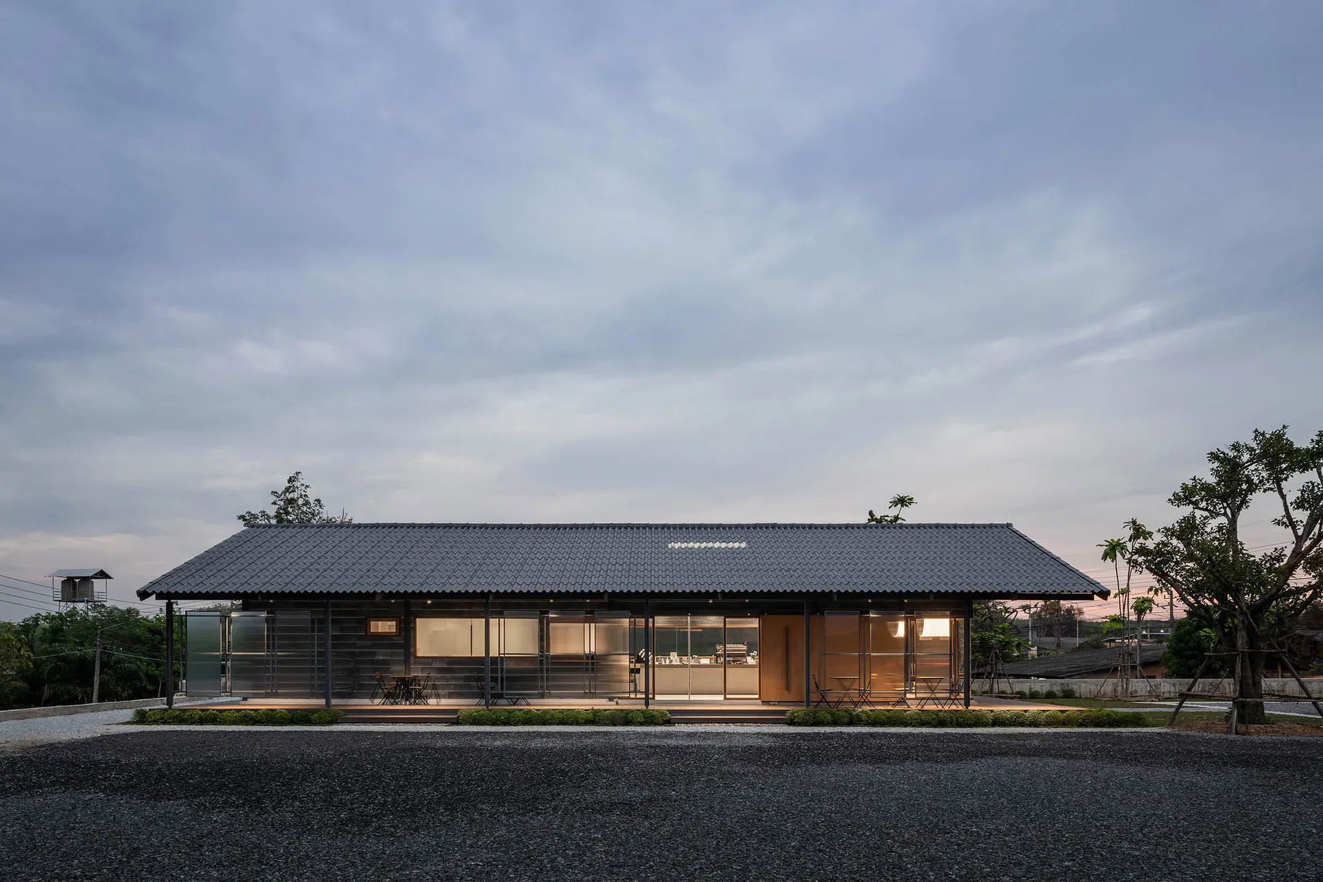 A minimalist outdoor café with a metal roof, tables, and chairs under the open sky.